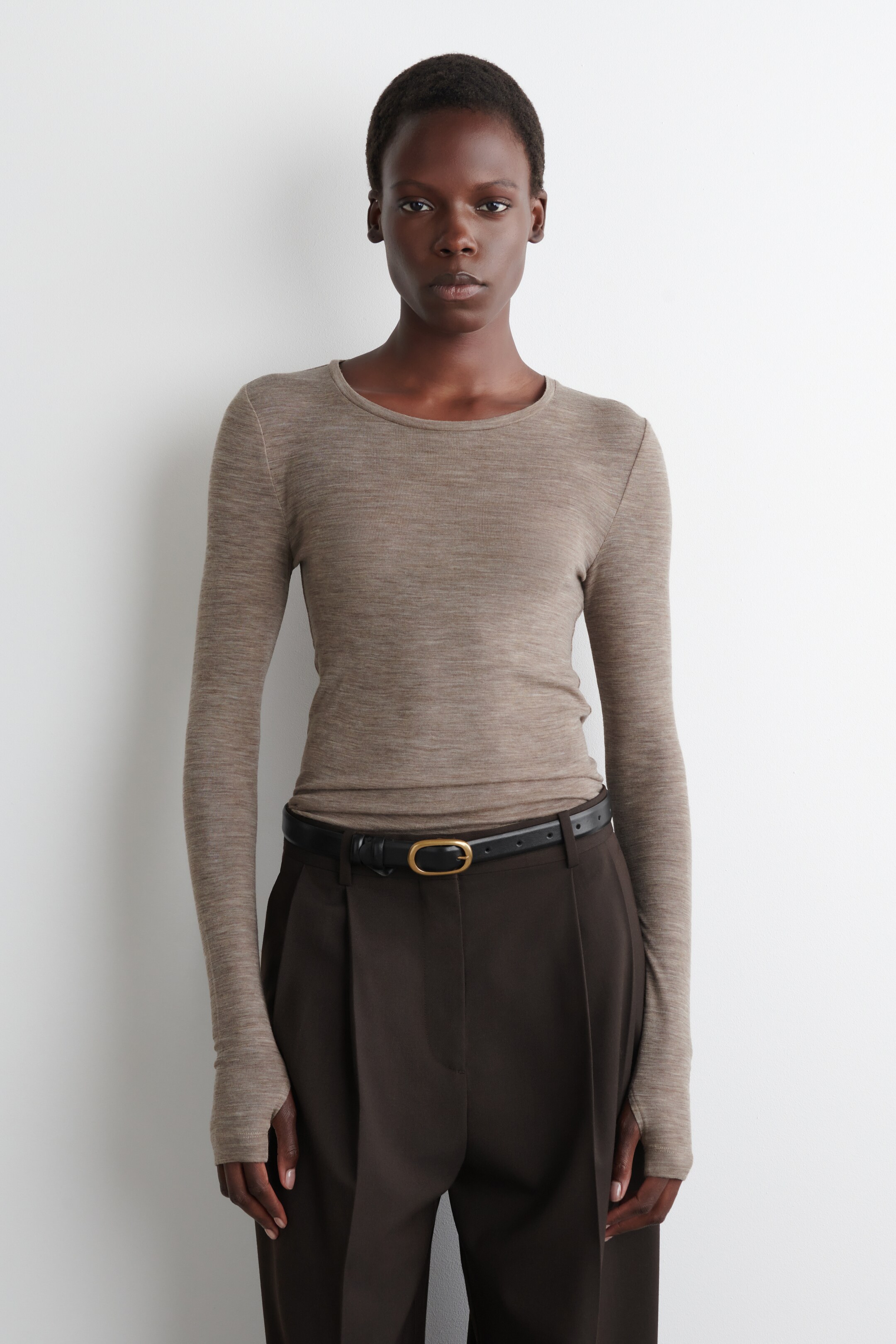 View larger image: A heathered light brown fine knit long-sleeved top is being presented front-facing. It is showcasing a crew neck and long, slim-fit sleeves that are extending over the hands with thumbholes, and is being worn tucked in to reveal its form-fitting silhouette.