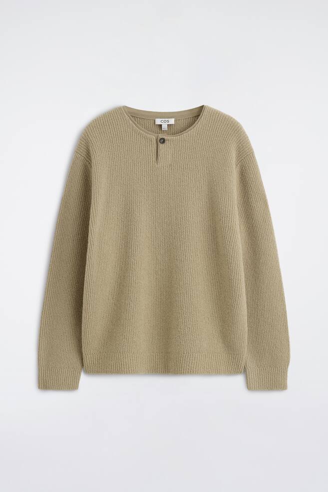 Beżowy sweter typu henley z dzianiny w prÄ
żek jest ustawiony przodem, ukazujÄ
c okrÄ
gÅy dekolt z pojedynczÄ
listwÄ
na guziki oraz obniżonÄ
liniÄ ramion. Sweter ma dÅugie rÄkawy z prÄ
żkowanymi mankietami oraz prosty, prÄ
żkowany dóÅ. - 1