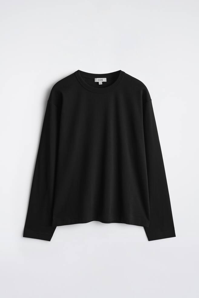 A black long-sleeve top is showcased front-facing, featuring a ribbed crew neck and a straight hem. The smooth fabric drapes loosely, with a white brand tag visible at the back of the neck. - 1