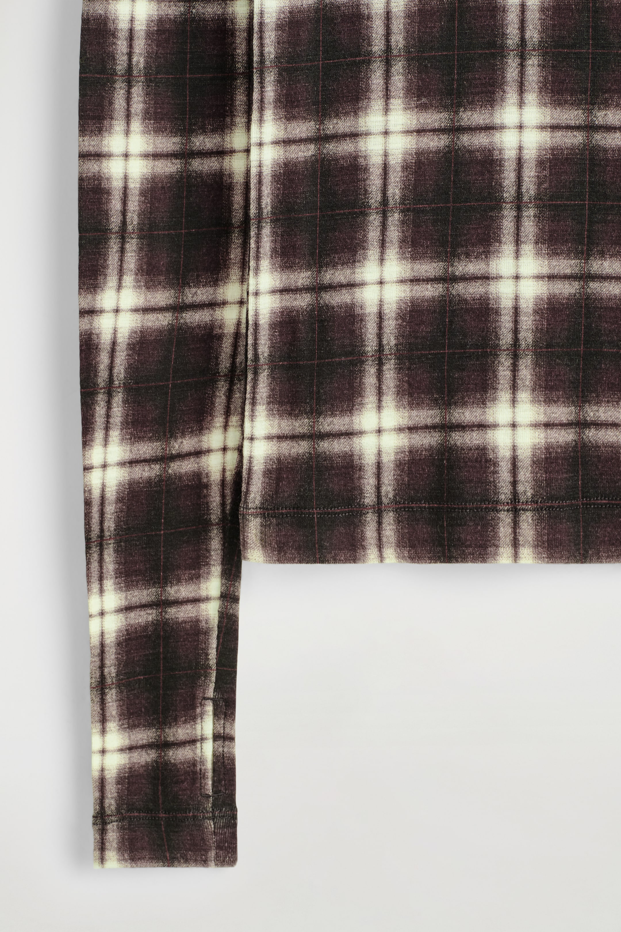 Agrandir l'image: Un vêtement présente un gros plan de son tissu en maille douce, avec un motif à carreaux marron foncé et crème, agrémenté de fines lignes rougeâtres, visible sur une manche longue et l'ourlet du bas.