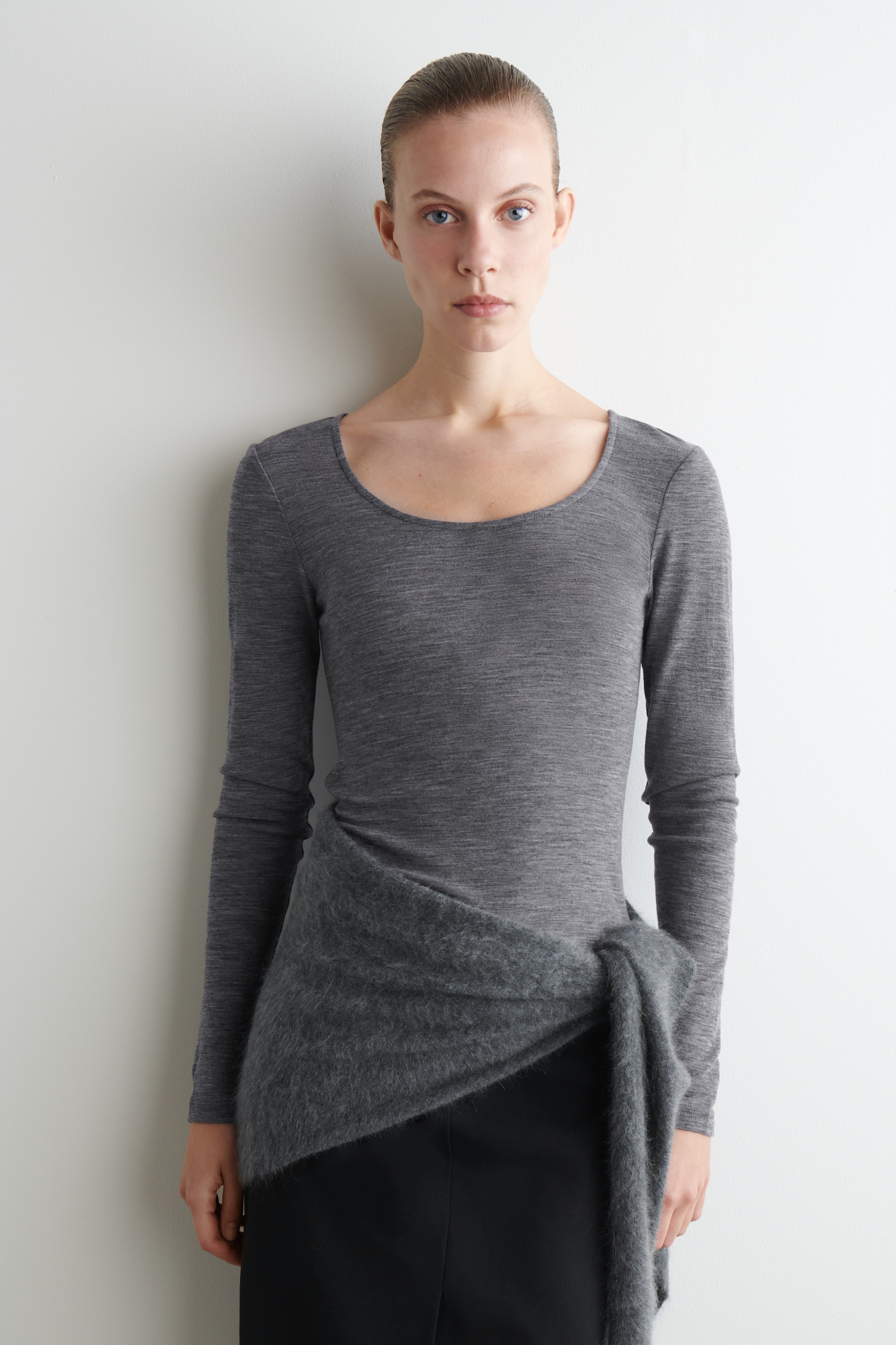 Grösseres Bild ansehen: Das grau-melierte Langarmshirt, von vorne gezeigt, hat einen sanft geschwungenen Ausschnitt und eine schmale Passform mit einer fein gestrickten Textur.