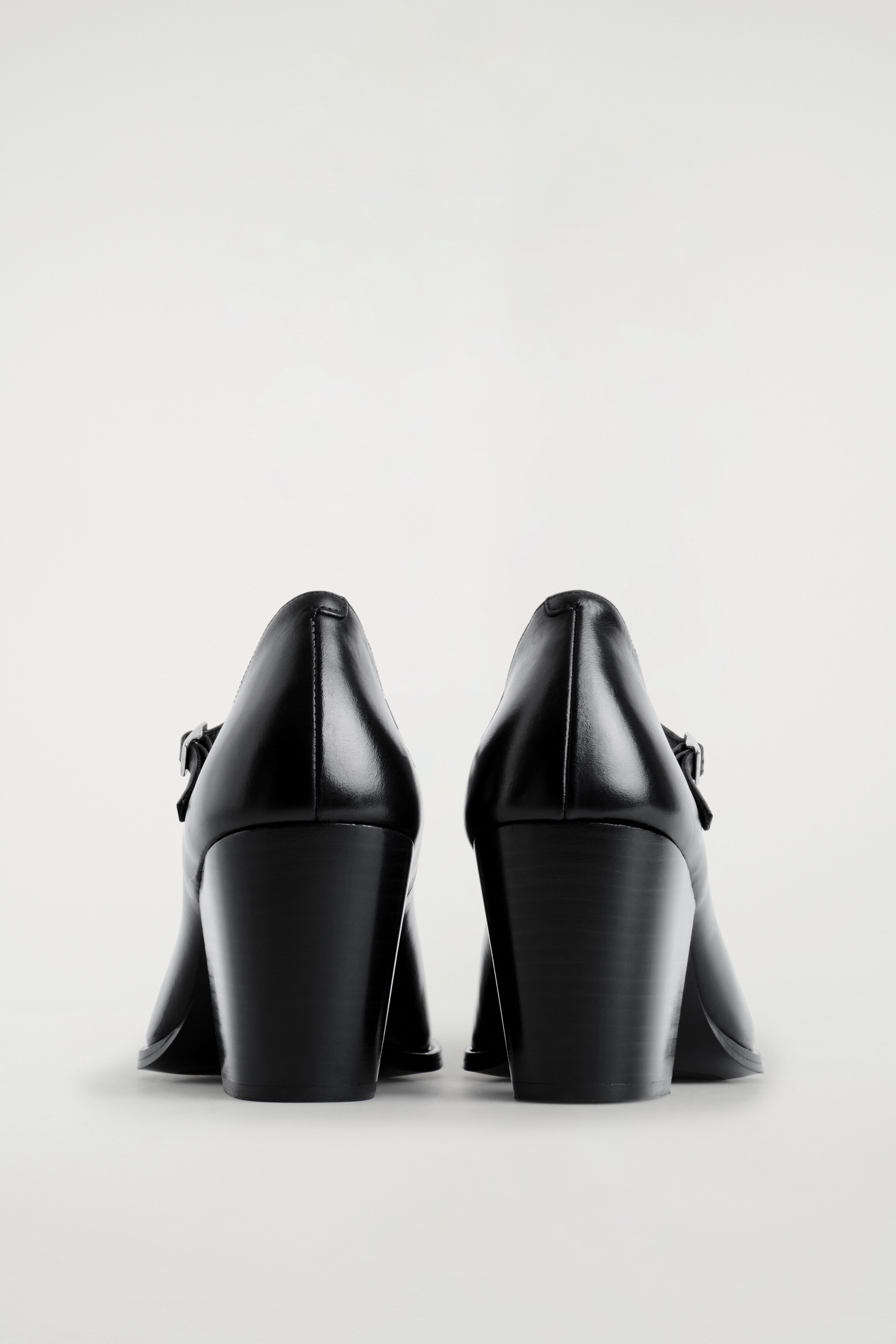 Agrandir l'image: Deux chaussures Mary Jane à talons en cuir noir sont présentées de l'arrière, mettant en valeur leurs talons blocs larges et de hauteur moyenne avec une texture empilée visible. Un détail de boucle est visible sur le côté de chaque tige en cuir lisse.