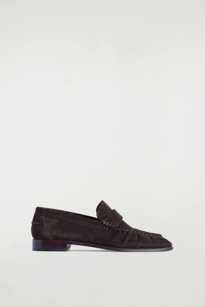 Ein dunkelbrauner Wildleder-Loafer präsentiert sein Seitenprofil, mit einer Mokassin-Nahtkonstruktion und sichtbaren Nähten, einem Riemen über dem Spann und einem niedrigen Blockabsatz. - 1