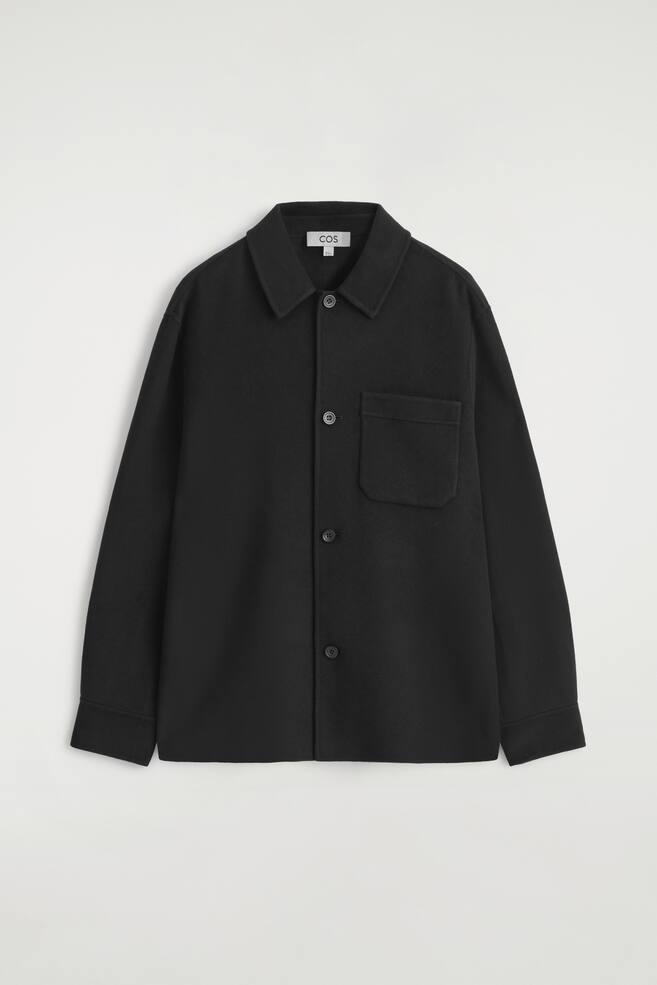 A black, relaxed-fit overshirt is presented from the FRONT, featuring a pointed collar, a front button closure with four visible buttons, and a single patch pocket on the left chest. It has long sleeves with buttoned cuffs. - 1