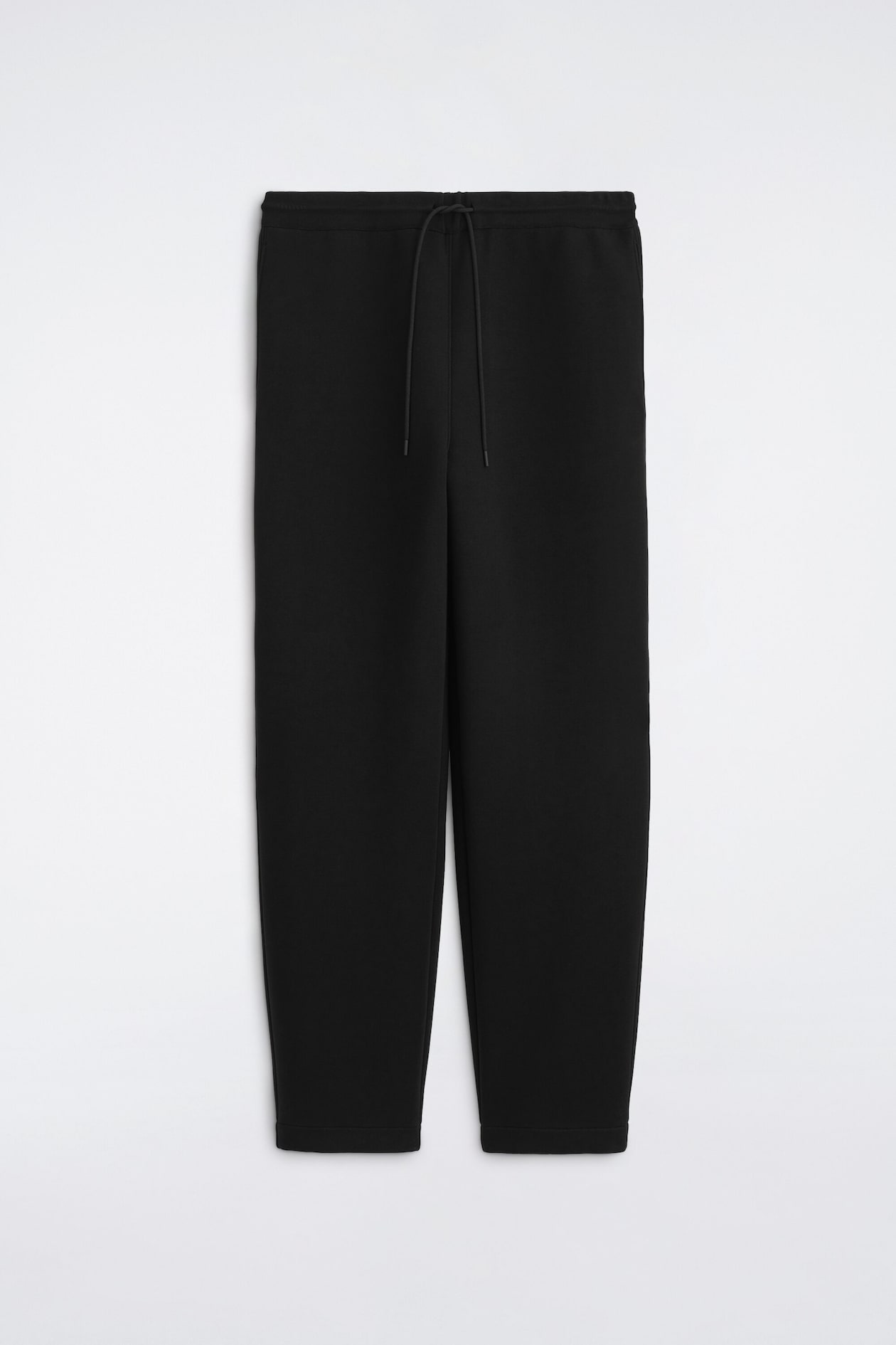 Black sweatpants are shown from the front, featuring an elasticized waistband with an adjustable matching drawstring. The pants showcase a relaxed, slightly tapered leg design with clean-finished hems.