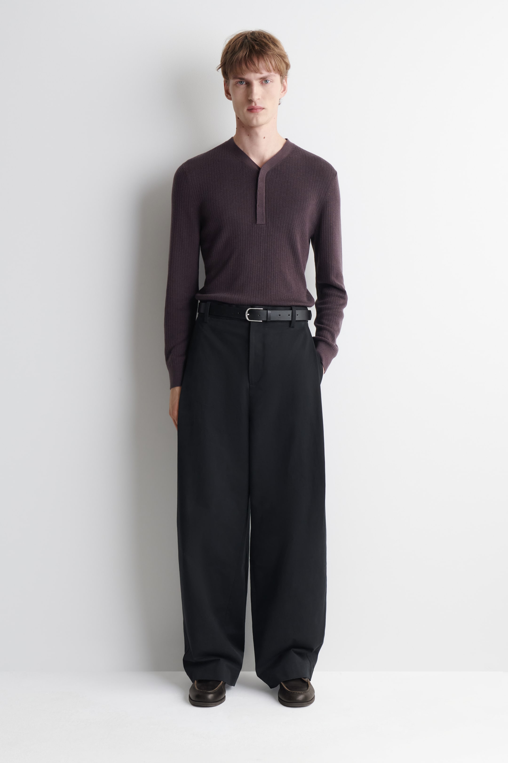 Größeres Bild ansehen: Dunkelbraune Leder-Bootsschuhe mit tonalen Lederbändern und gesteppten Aprons werden vom Model getragen.