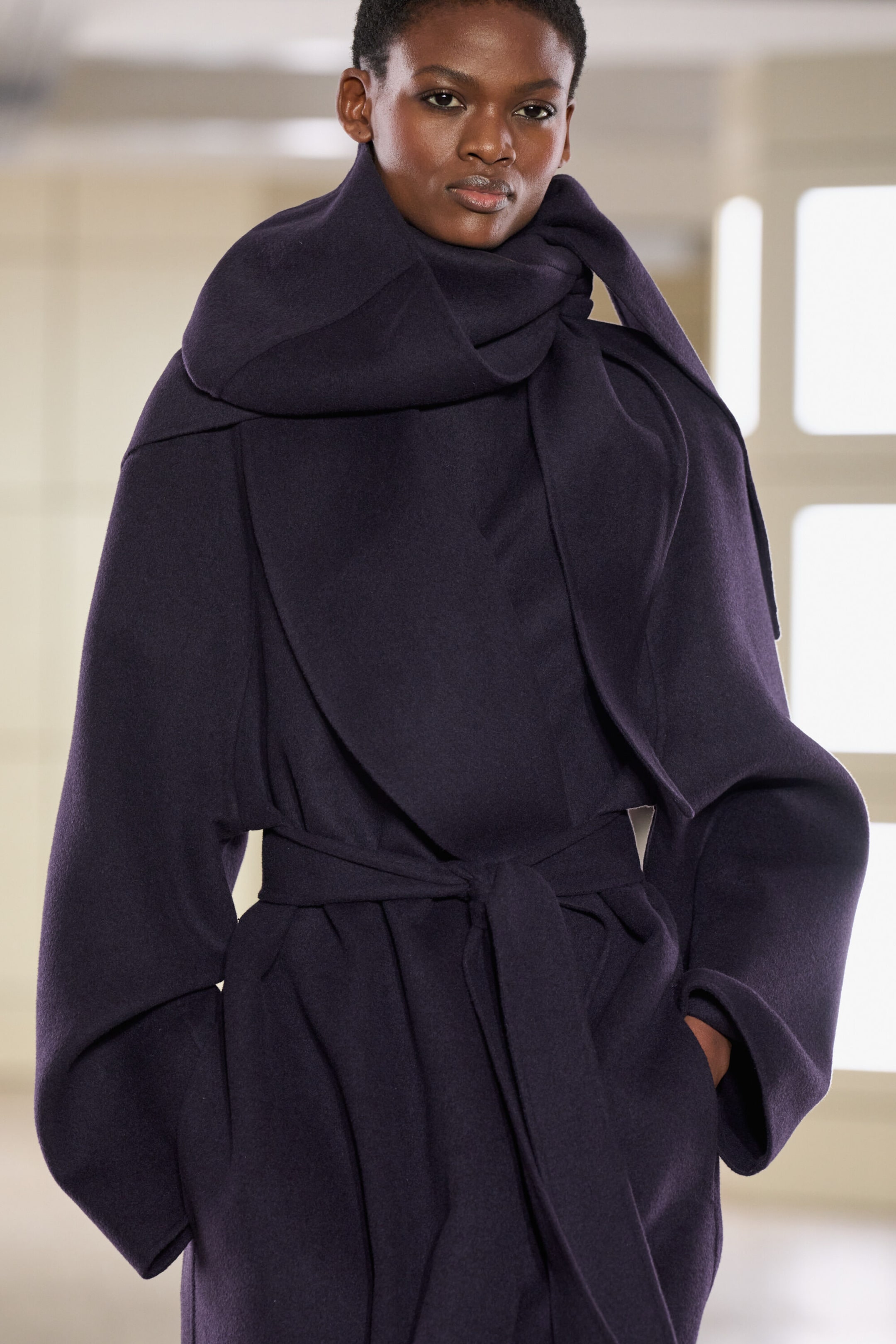 The double-faced wool shawl-collar coat in a deep plum colour is showcasing a voluminous, draped collar wrapped around the neck. Seen from the front, the coat features wide, relaxed sleeves and a matching tie belt cinched at the waist. The double-faced wool shawl-collar coat in a deep plum colour is showcasing a voluminous, draped collar wrapped around the neck. Seen from the front, the coat features wide, relaxed sleeves and a matching tie belt cinched at the waist.