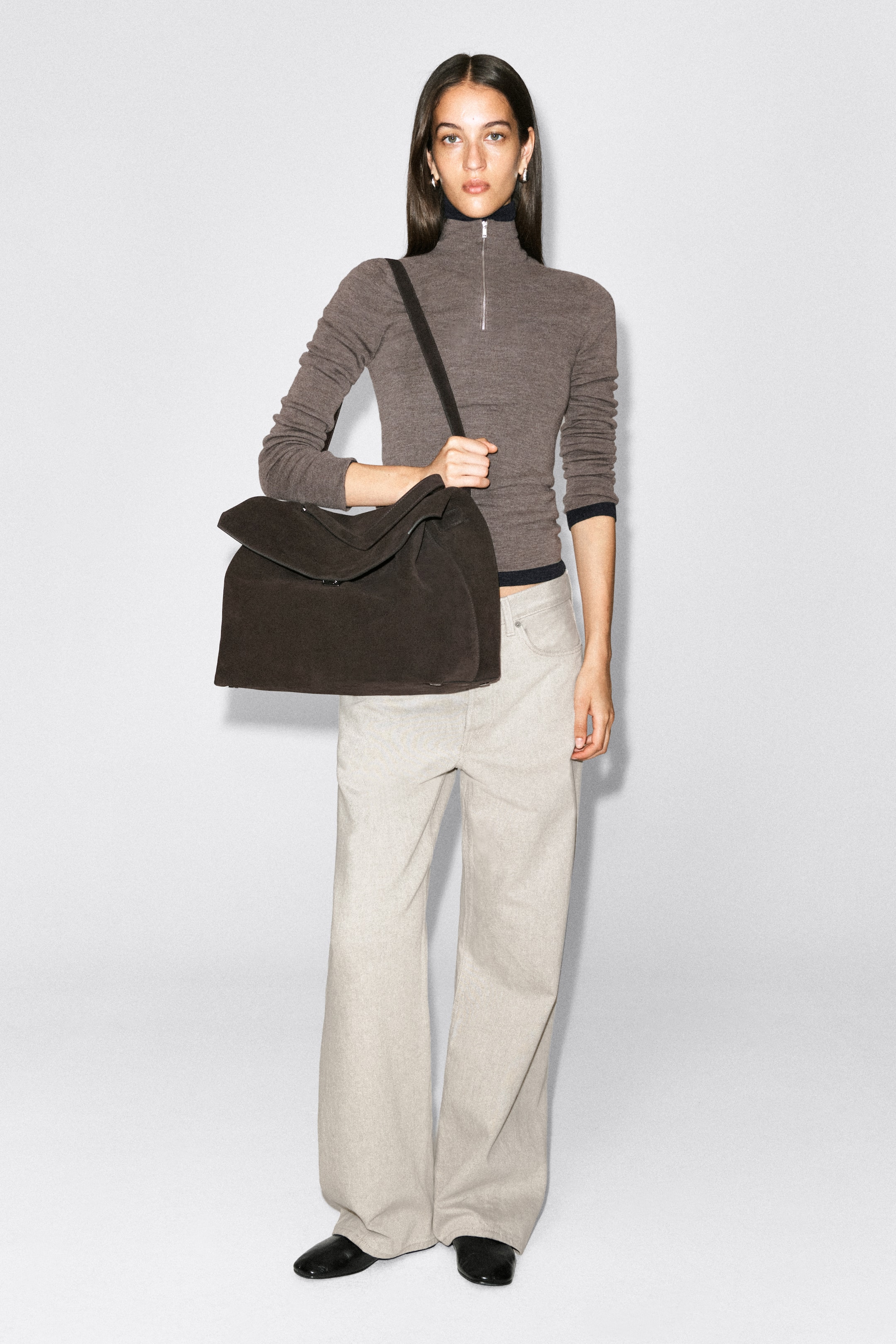 Zobrazit větší obrázek: Kabelka Trullo Oversized Flap Bag z tmavě hnědé kůže je nošena modelkou přes rameno, přičemž drží plochý ramenní popruh. Kabelka má ležérní, měkkou strukturu s velkou přehnutou přední klopou.