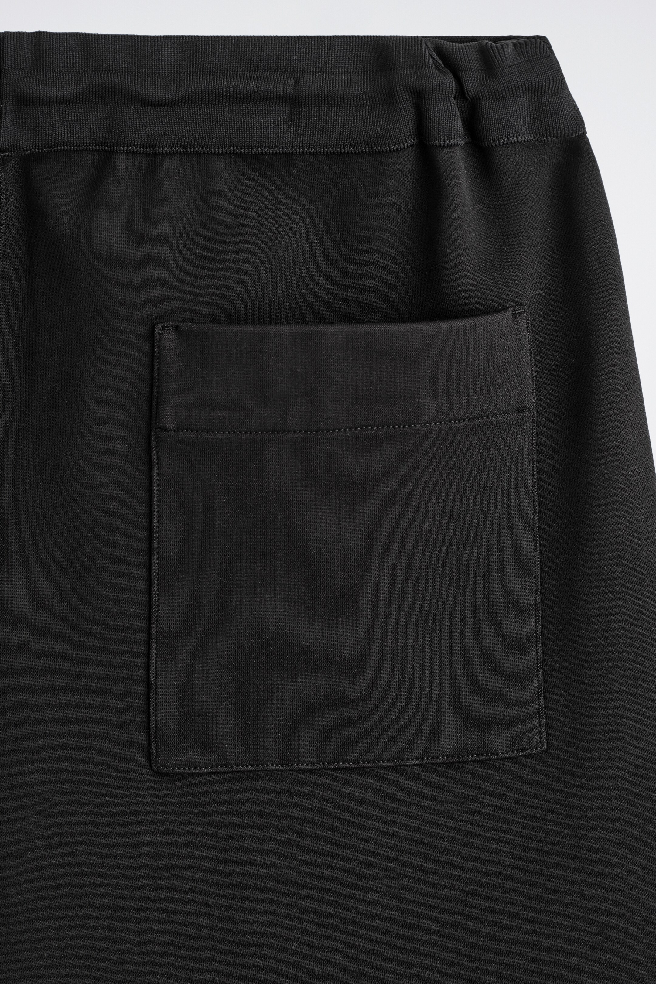 Agrandir l'image: Des joggeurs noirs sont montrés de dos, avec une large ceinture côtelée. Une grande poche plaquée rectangulaire, détaillée avec une ligne de couture horizontale près du haut, est visible à l'arrière.
