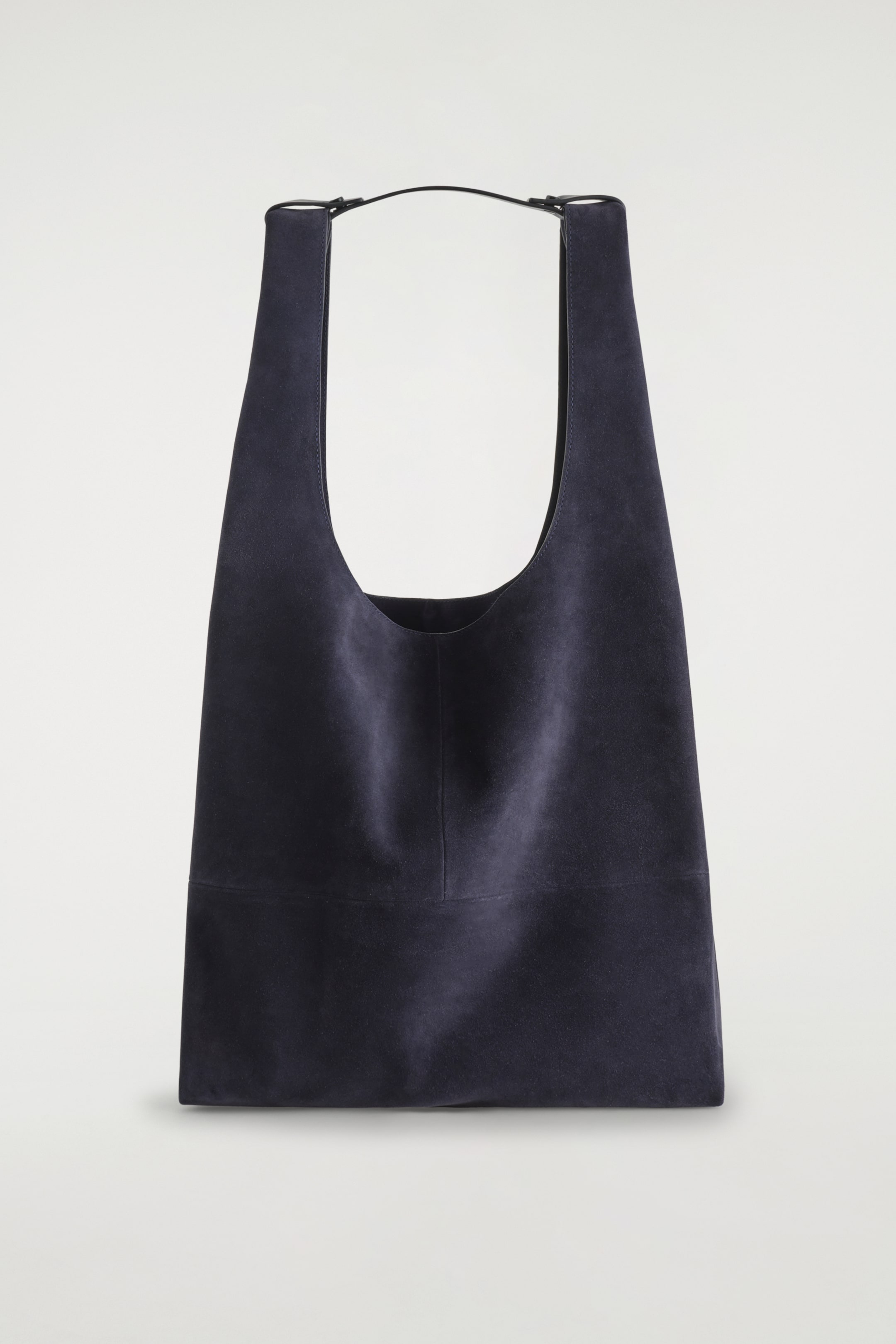 Visualizza immagine più grande: Una borsa shopper in camoscio grigio scuro è presentata FRONTALE, caratterizzata da una forma alta e morbida con un'apertura a forma di U. Due tracolle in pelle nera sono attaccate alla parte superiore della borsa e sono tenute insieme da una linguetta centrale in pelle, mentre una cucitura verticale corre lungo la parte anteriore con una cucitura orizzontale visibile vicino al fondo.