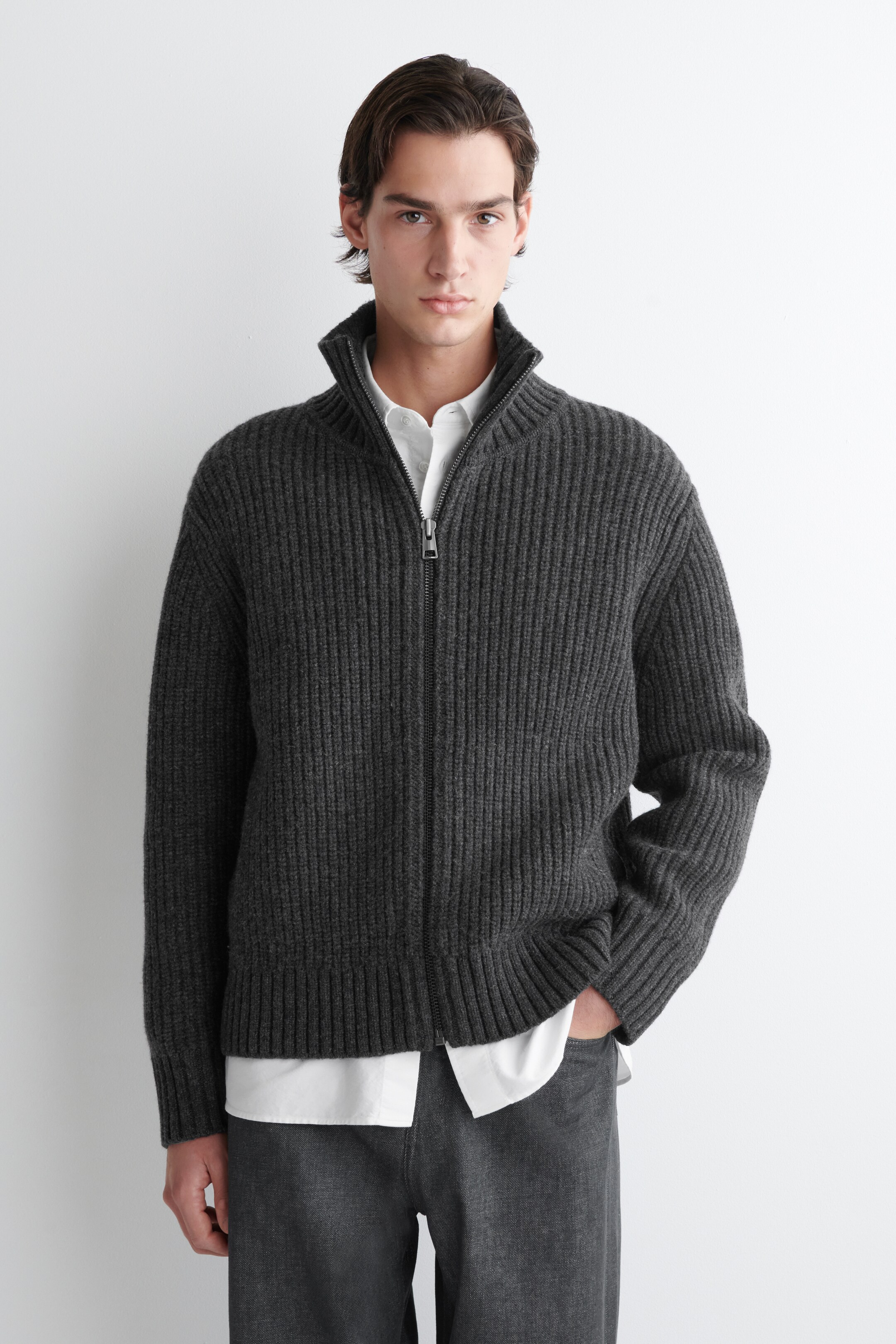Agrandir l'image: Un cardigan zippé intégral côtelé gris foncé est présenté de face, avec un col montant et des manches longues avec des poignets et un ourlet côtelés, et il est visiblement superposé sur une chemise blanche à col.