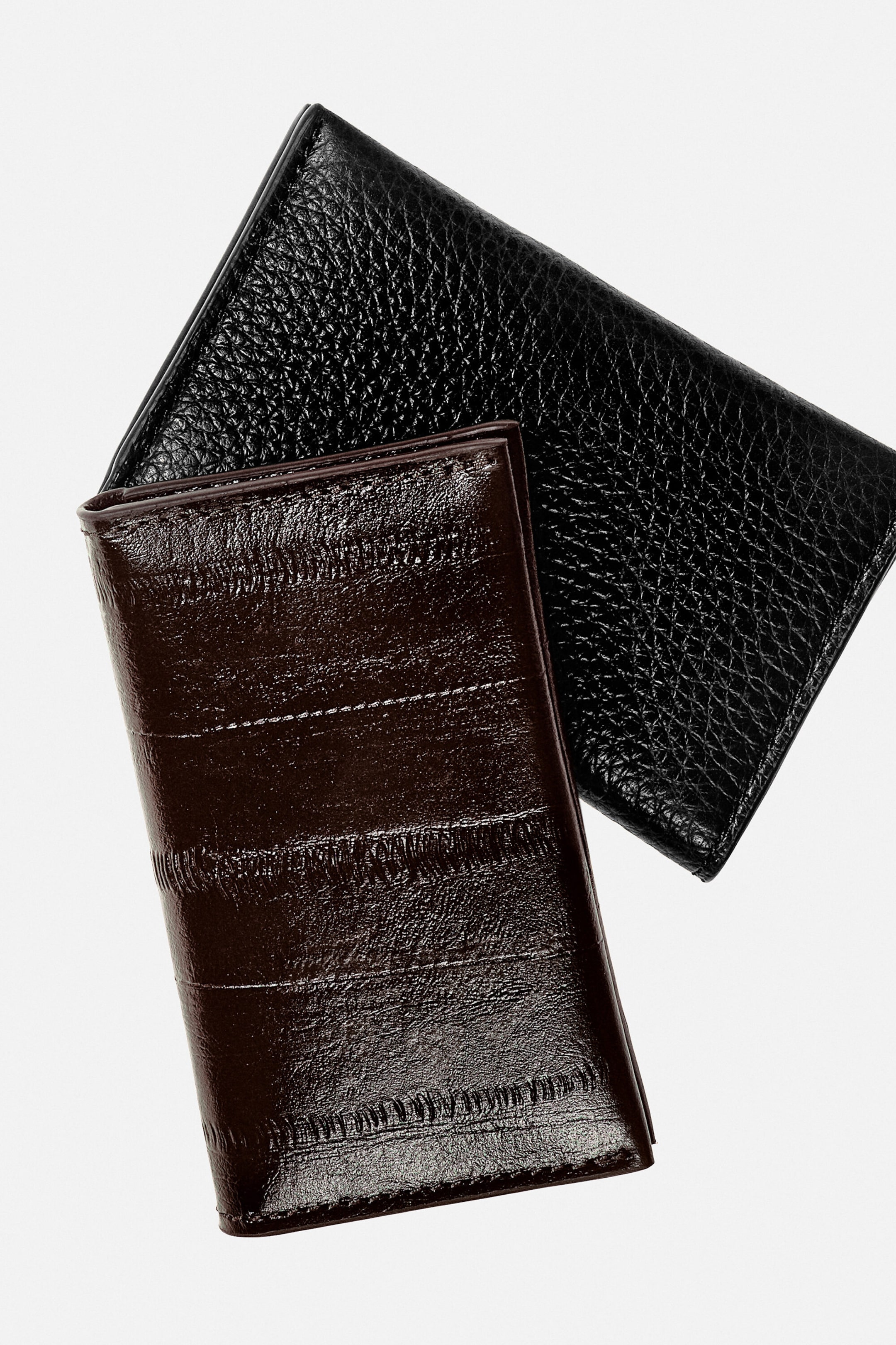 A black leather card holder and a dark brown leather card holder are overlapping to show their distinct textures from the front. The black card holder showcases a pebbled leather finish, while the dark brown card holder displays a glossy, horizontally paneled design. A black leather card holder and a dark brown leather card holder are overlapping to show their distinct textures from the front. The black card holder showcases a pebbled leather finish, while the dark brown card holder displays a glossy, horizontally paneled design.