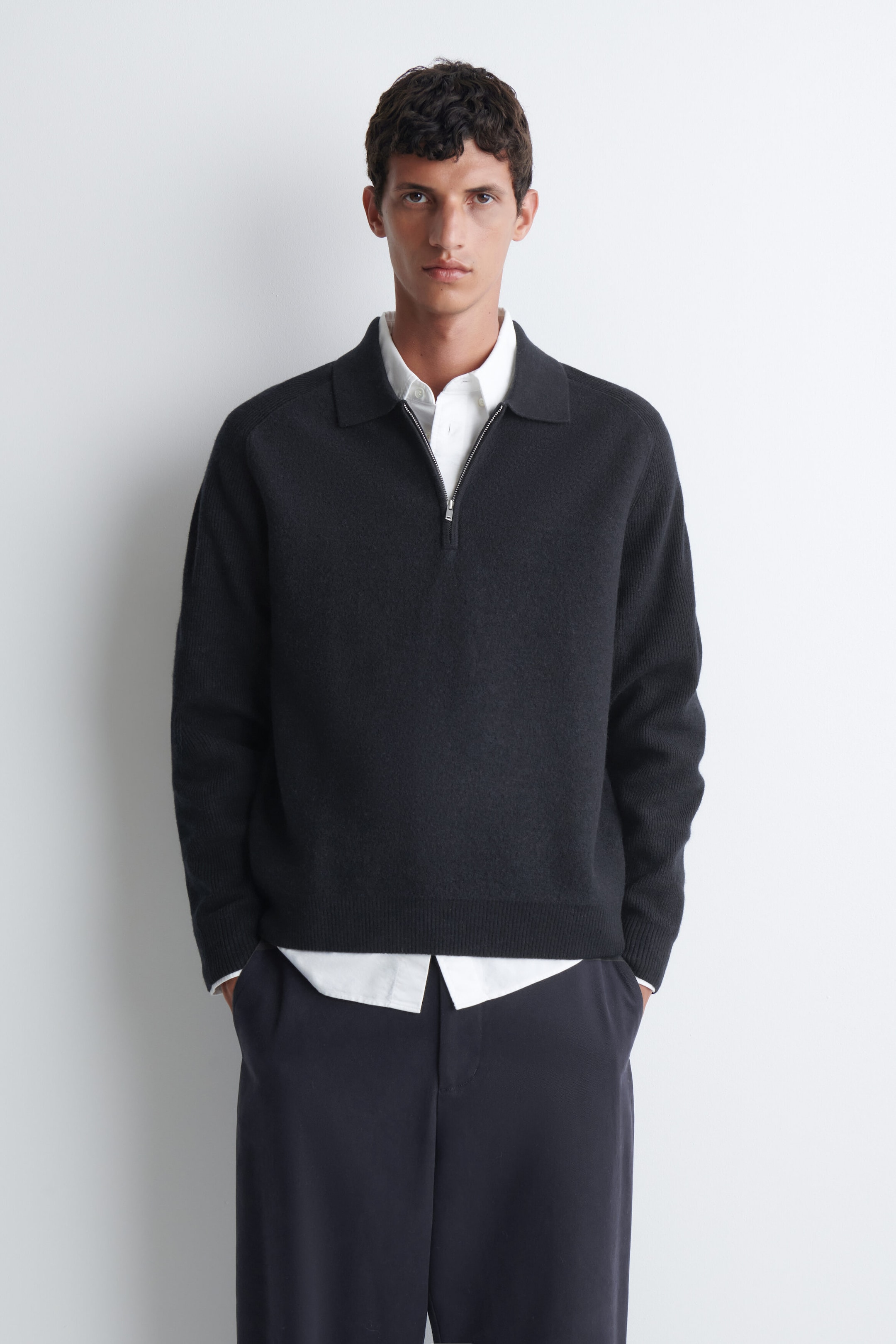 The model is wearing a dark grey panelled boiled-wool zip-up jumper, featuring a polo collar, a silver-tone half-zip, and ribbed trims. The jumper is layered over a white collared shirt and styled with dark trousers. The model is wearing a dark grey panelled boiled-wool zip-up jumper, featuring a polo collar, a silver-tone half-zip, and ribbed trims. The jumper is layered over a white collared shirt and styled with dark trousers.