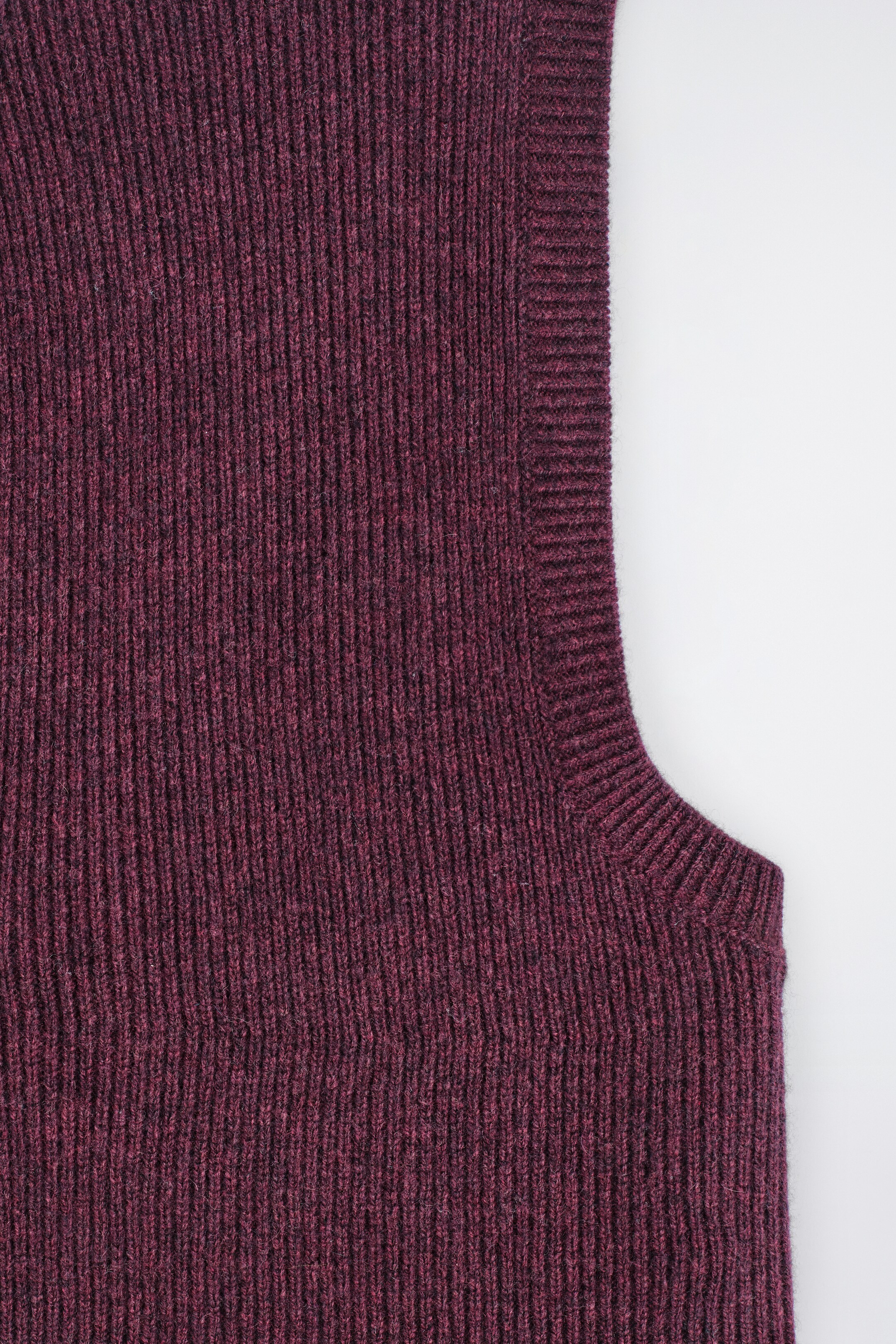 View larger image: A dark reddish-purple balaclava is being presented in a close-up, showing its fine rib-knitted texture and a wider ribbed edge defining a curved opening on the garment.