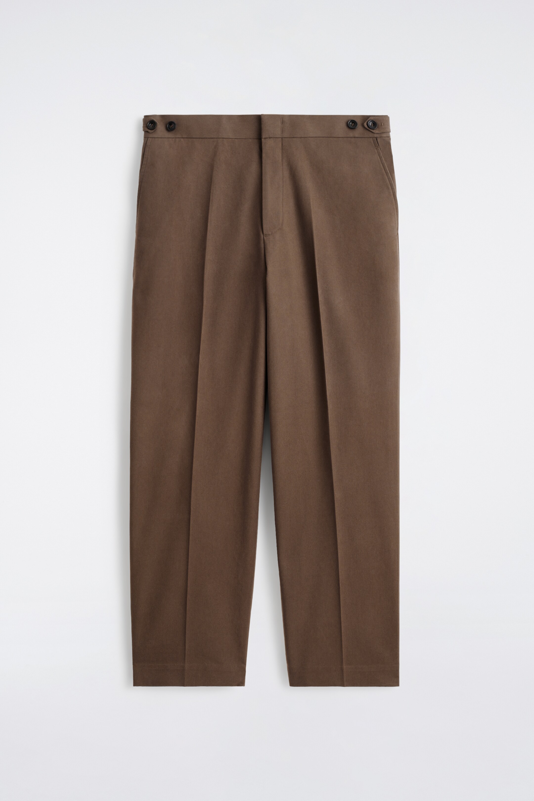 Agrandir l'image: Le DEVANT du pantalon marron foncé est présenté, avec une coupe droite et raccourcie, ornée de plis centraux descendant le long de chaque jambe. Des pattes boutonnées détaillent la taille, accompagnées d'une fermeture éclair visible et de poches latérales.