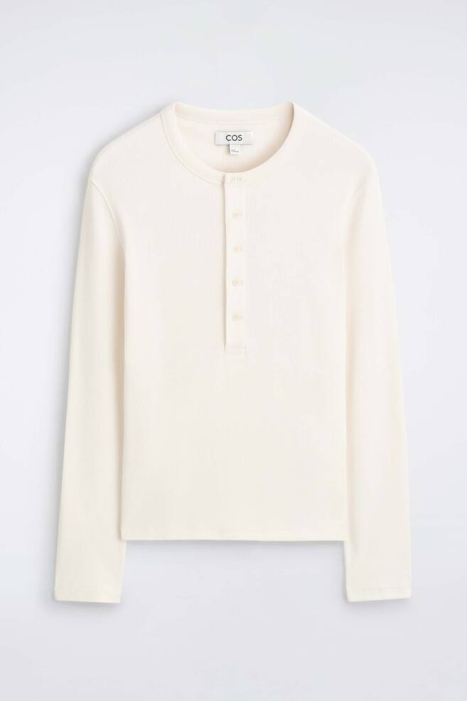 Un t-shirt Henley slim en coton cÃ´telÃ© Ã  manches longues est prÃ©sentÃ© de face, en couleur blanc cassÃ©, avec un col rond et une patte de boutonnage centrale sur le devant dotÃ©e de cinq boutons assortis. Le vÃªtement prÃ©sente une fine texture cÃ´telÃ©e sur lâensemble du corps et des manches longues. - 1