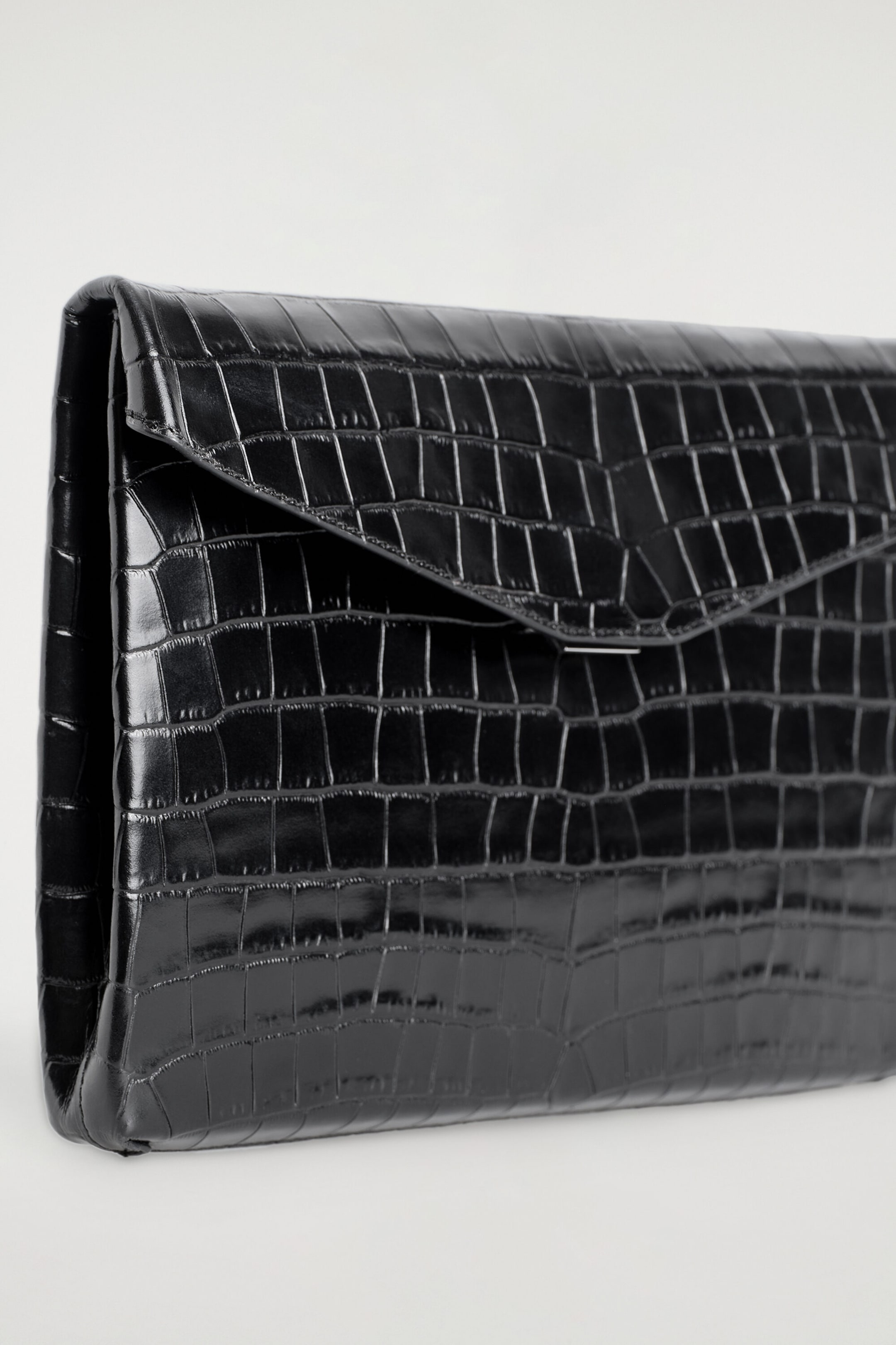 A black croc-effect leather envelope clasp pouch rests at a three-quarter front angle, showcasing its structured rectangular design and glossy, textured finish. The pouch features a pointed envelope-style front flap with a discreet silver-tone metal clasp. A black croc-effect leather envelope clasp pouch rests at a three-quarter front angle, showcasing its structured rectangular design and glossy, textured finish. The pouch features a pointed envelope-style front flap with a discreet silver-tone metal clasp.