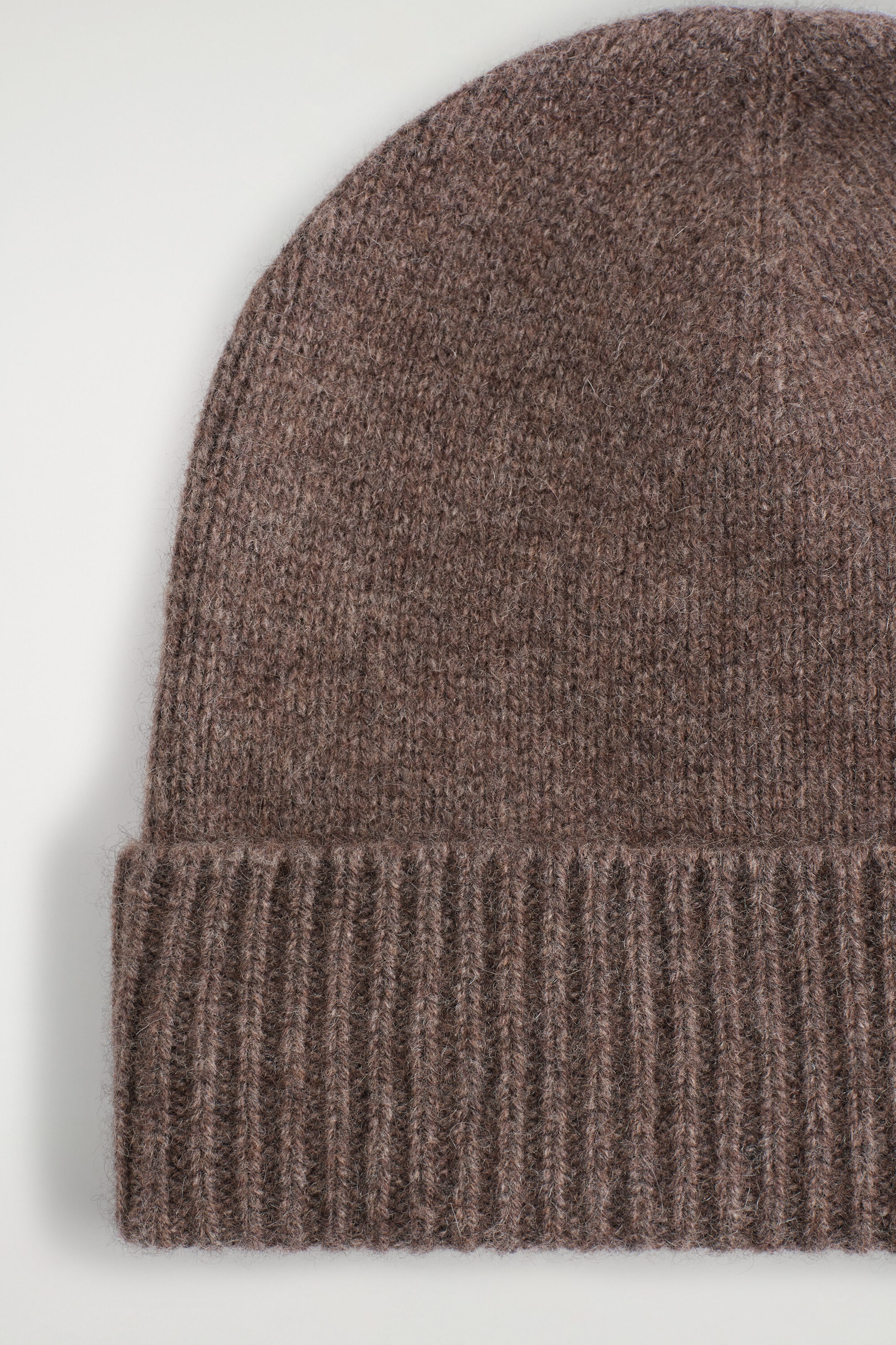 Un bonnet en cachemire brun présente une texture tricotée douce et duveteuse, avec un revers épais côtelé replié, en gros plan de face.
