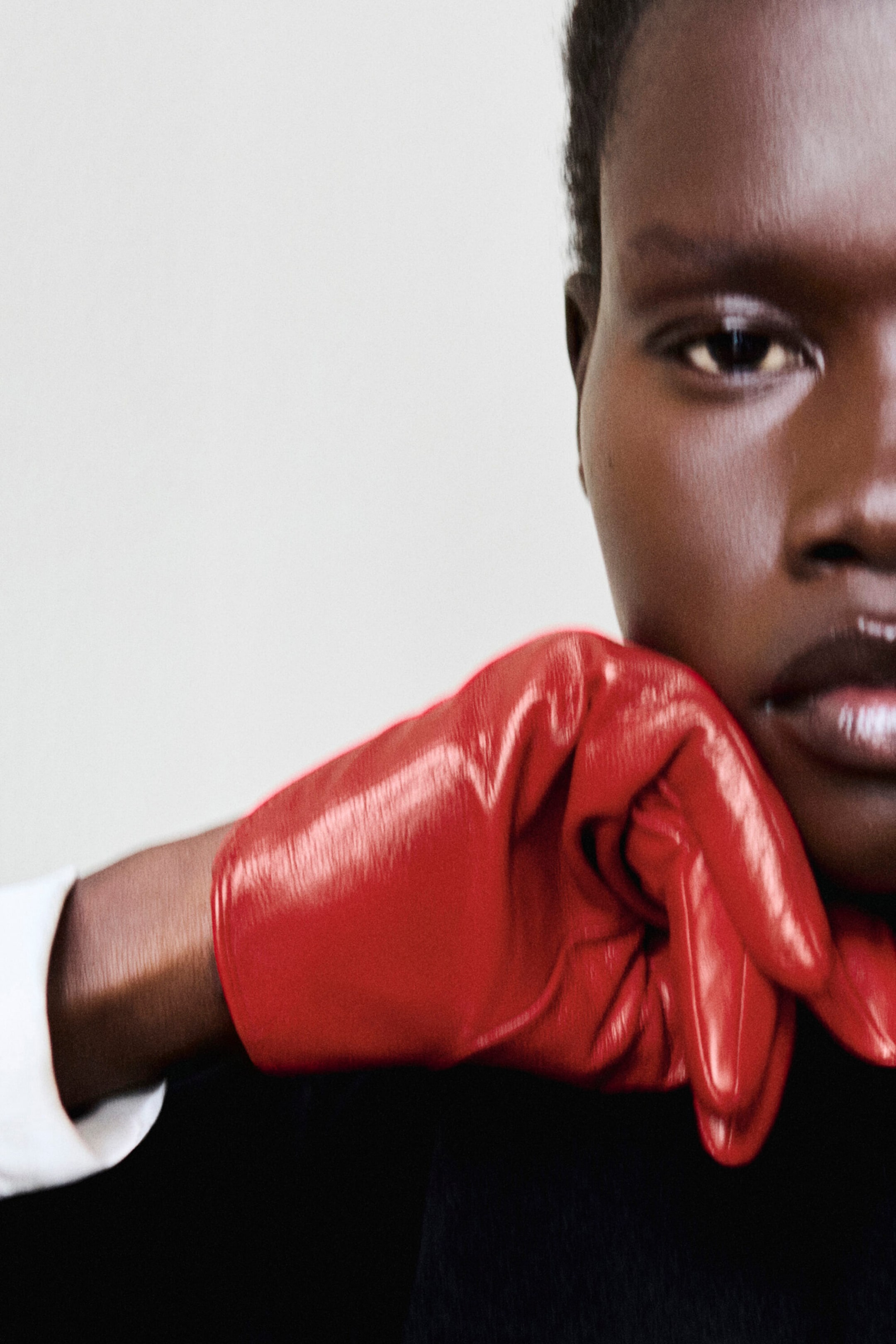 Red leather gloves with a glossy finish are worn on a hand resting against the chin, showcasing their snug fit and supple texture. The gloves display natural creasing and a smooth, reflective surface that highlights the quality of the leather. Red leather gloves with a glossy finish are worn on a hand resting against the chin, showcasing their snug fit and supple texture. The gloves display natural creasing and a smooth, reflective surface that highlights the quality of the leather.