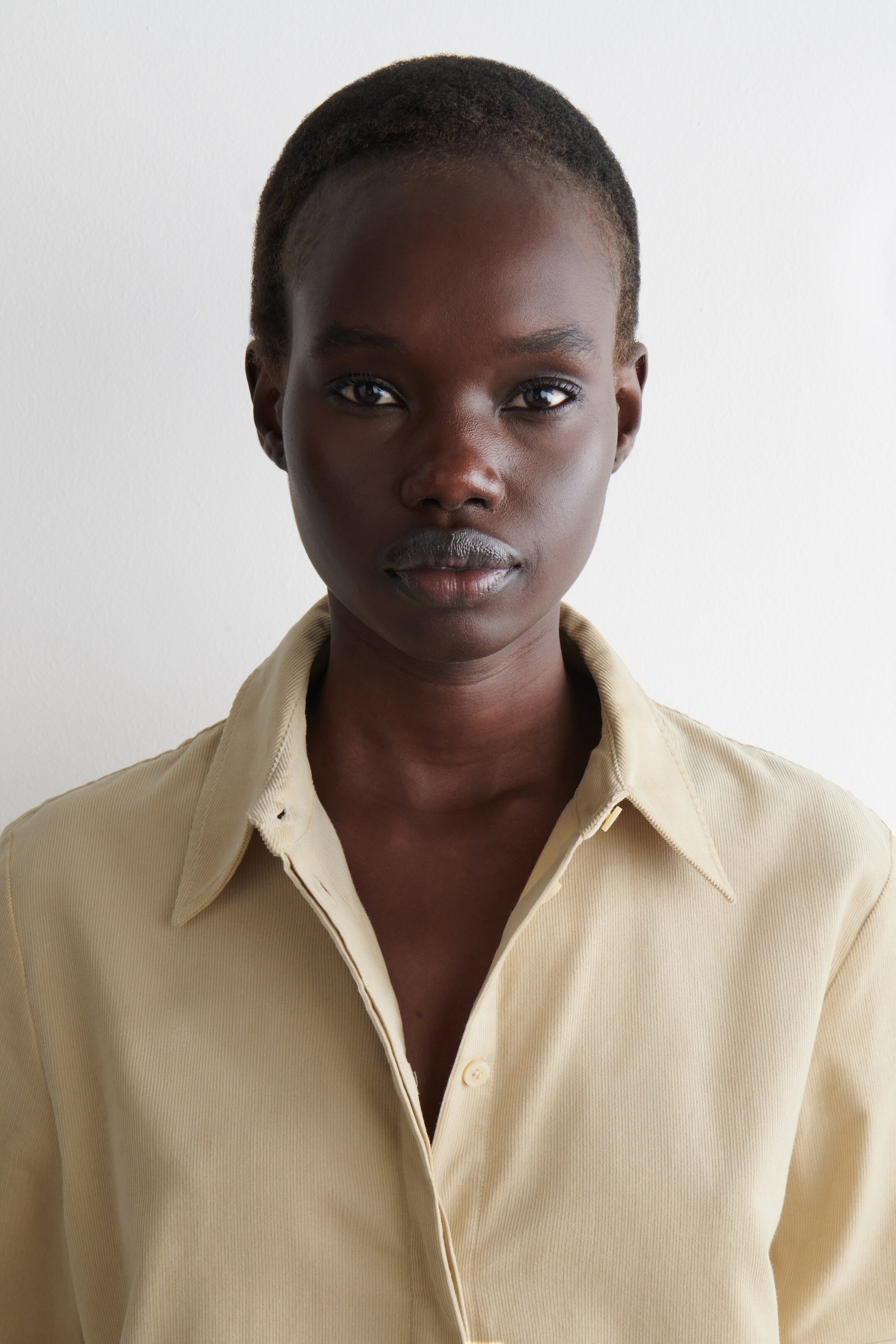 Agrandir l'image: Une chemise en velours côtelé beige clair est portée, avec un col classique à pointes et une patte de boutonnage avant avec des boutons visibles. La chemise est présentée partiellement déboutonnée.