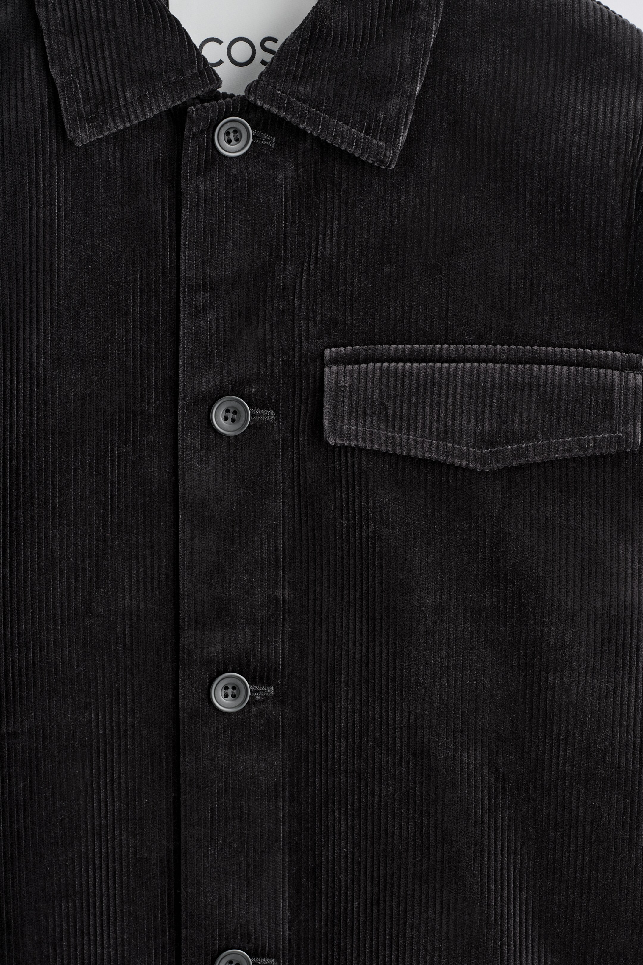 View larger image: A black corduroy overshirt is featuring a pointed collar, a central button closure with tonal buttons, and a single flap chest pocket on its front.