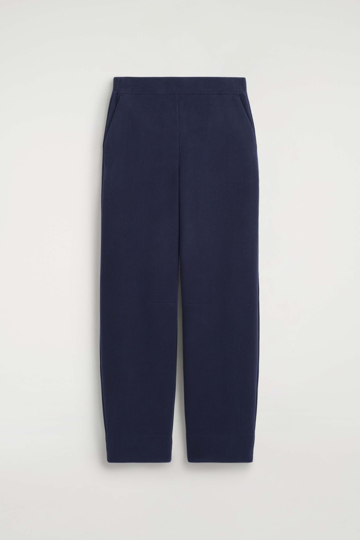 Le pantalon large en jersey de velours côtelé bleu marine est présenté de face, avec une taille élastique épurée et de discrètes poches latérales fendues. Le modèle met en valeur une texture finement côtelée et une silhouette droite décontractée.