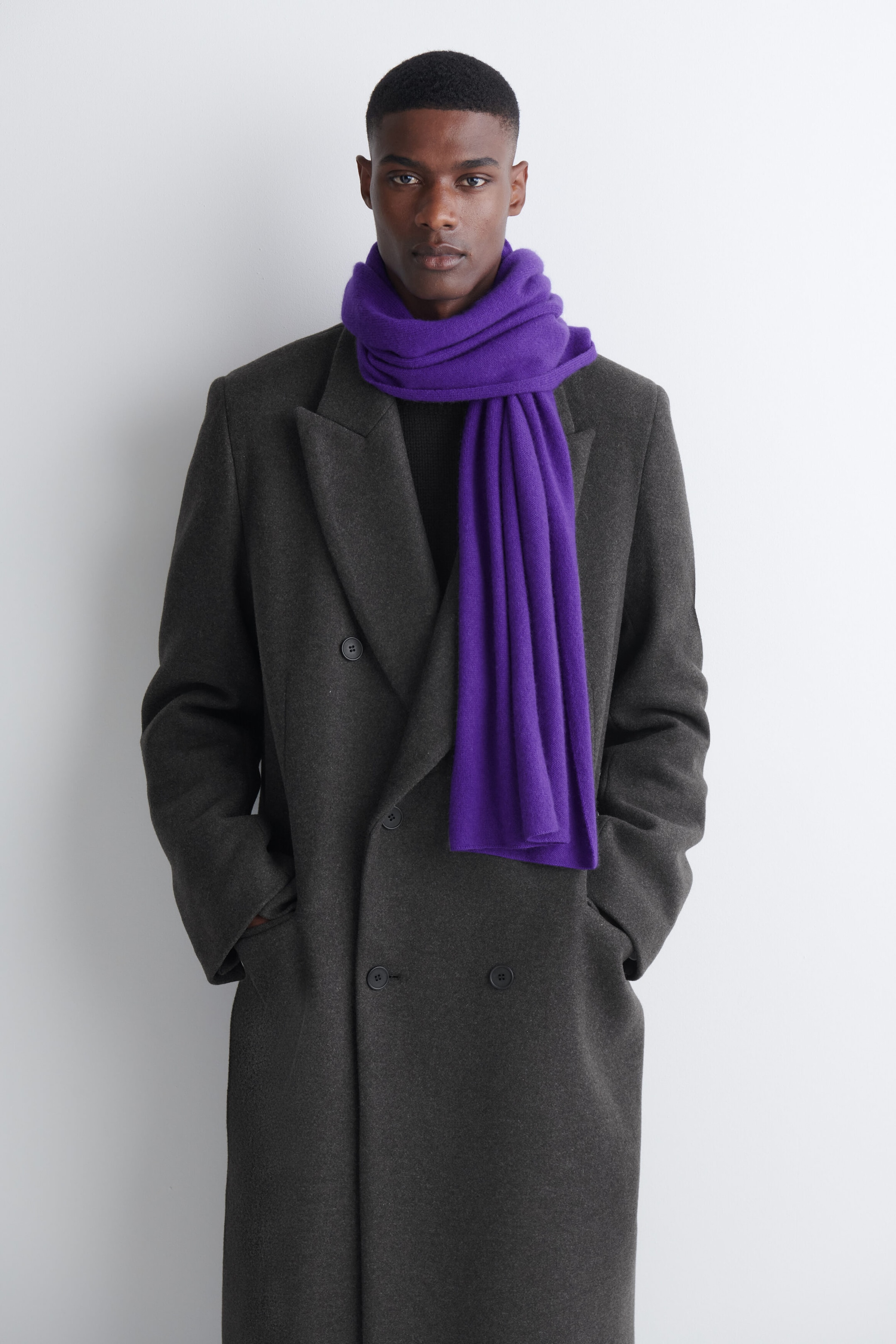 A purple cashmere scarf is being worn by the model, wrapped around the neck with one end draping down the front of a dark gray double-breasted coat. A purple cashmere scarf is being worn by the model, wrapped around the neck with one end draping down the front of a dark gray double-breasted coat.