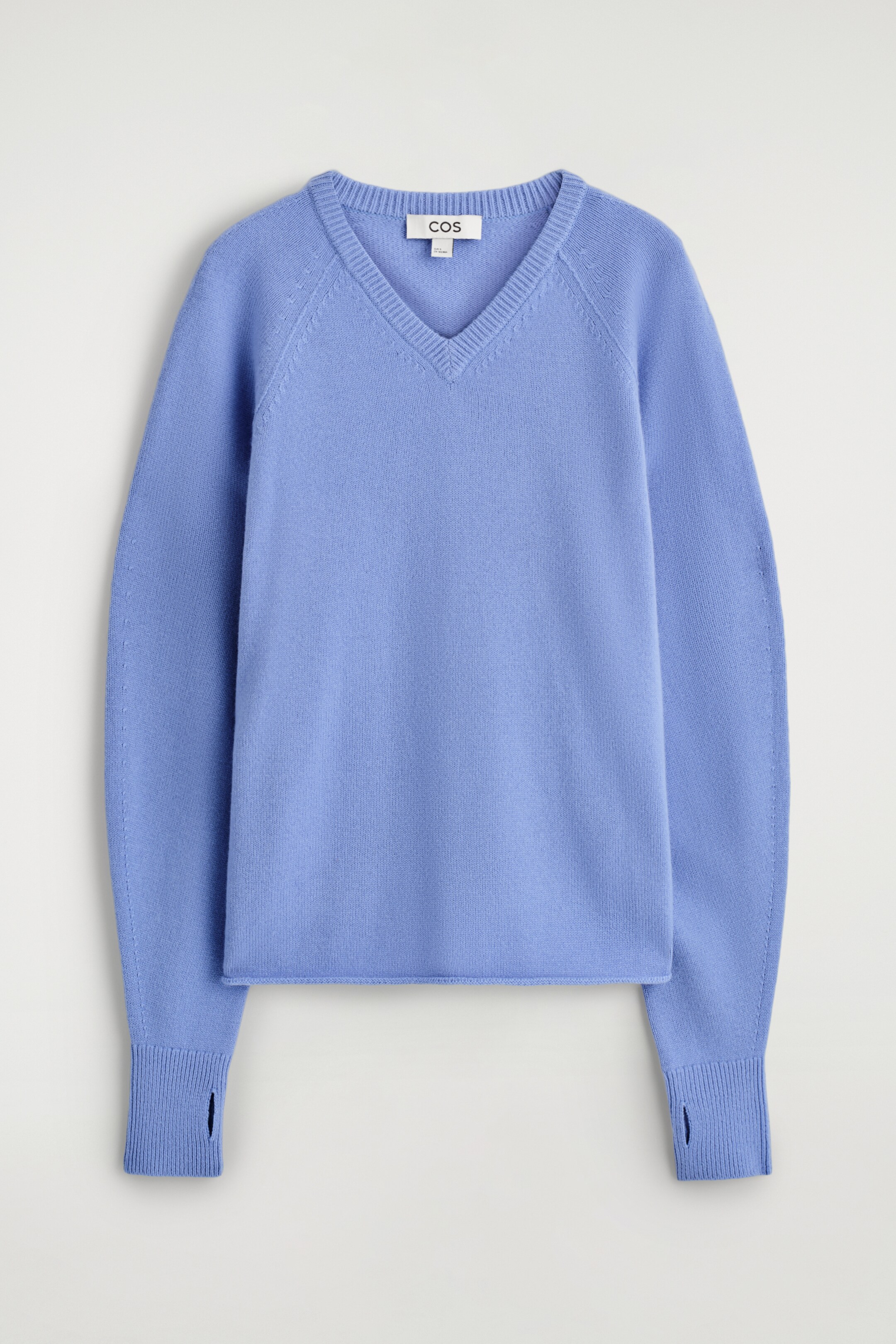 Ingrandisci l'immagine: Un maglione in lana merino blu pervinca è presentato frontalmente, con uno scollo a V a coste, maniche raglan e un orlo arrotolato. I polsini presentano ritagli per i pollici.