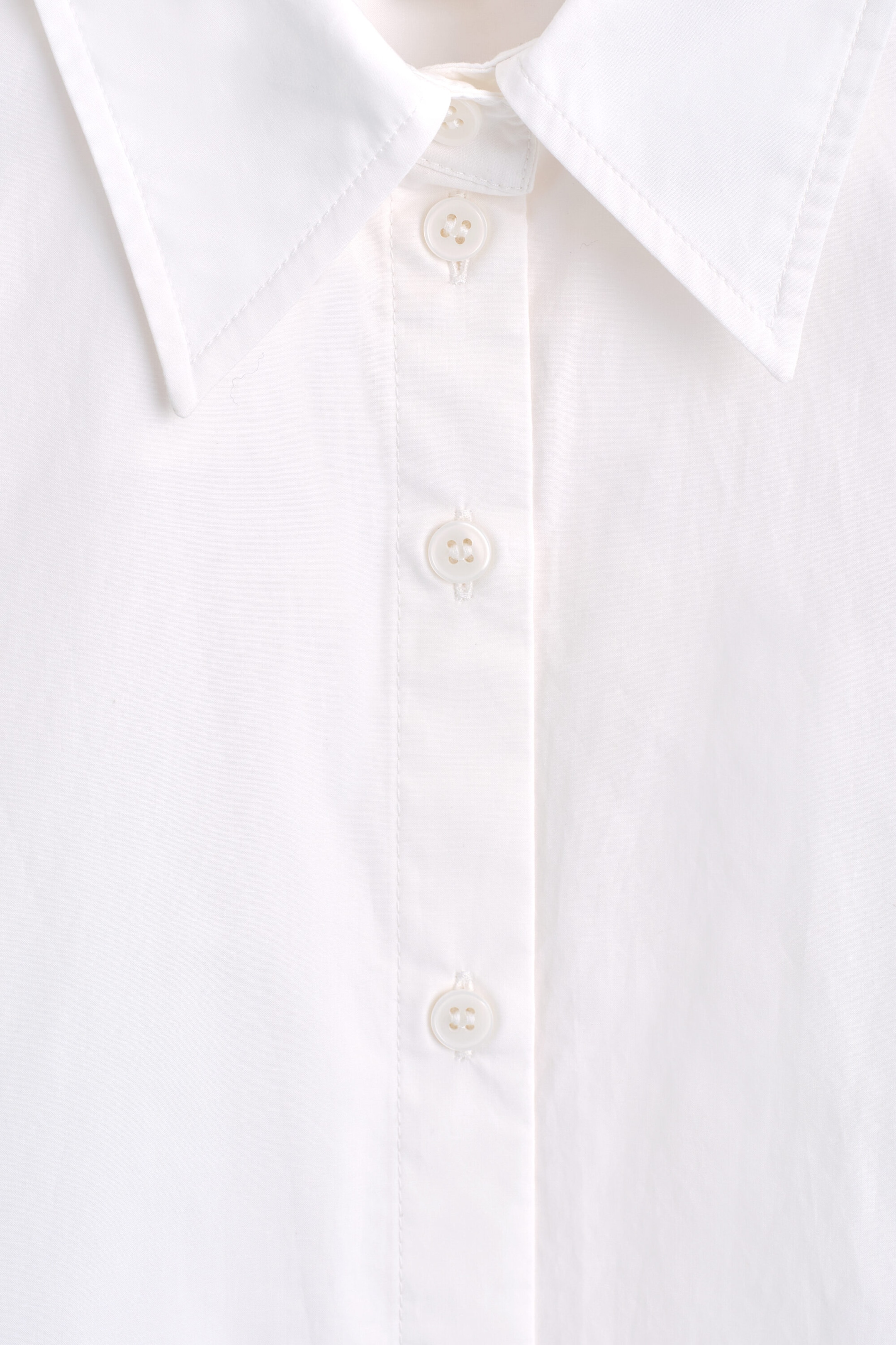 This close-up front view of the Classic Cotton-Poplin Shirt showcases its crisp white fabric, a structured pointed collar, and a central button-down placket featuring matching four-hole buttons. This close-up front view of the Classic Cotton-Poplin Shirt showcases its crisp white fabric, a structured pointed collar, and a central button-down placket featuring matching four-hole buttons.