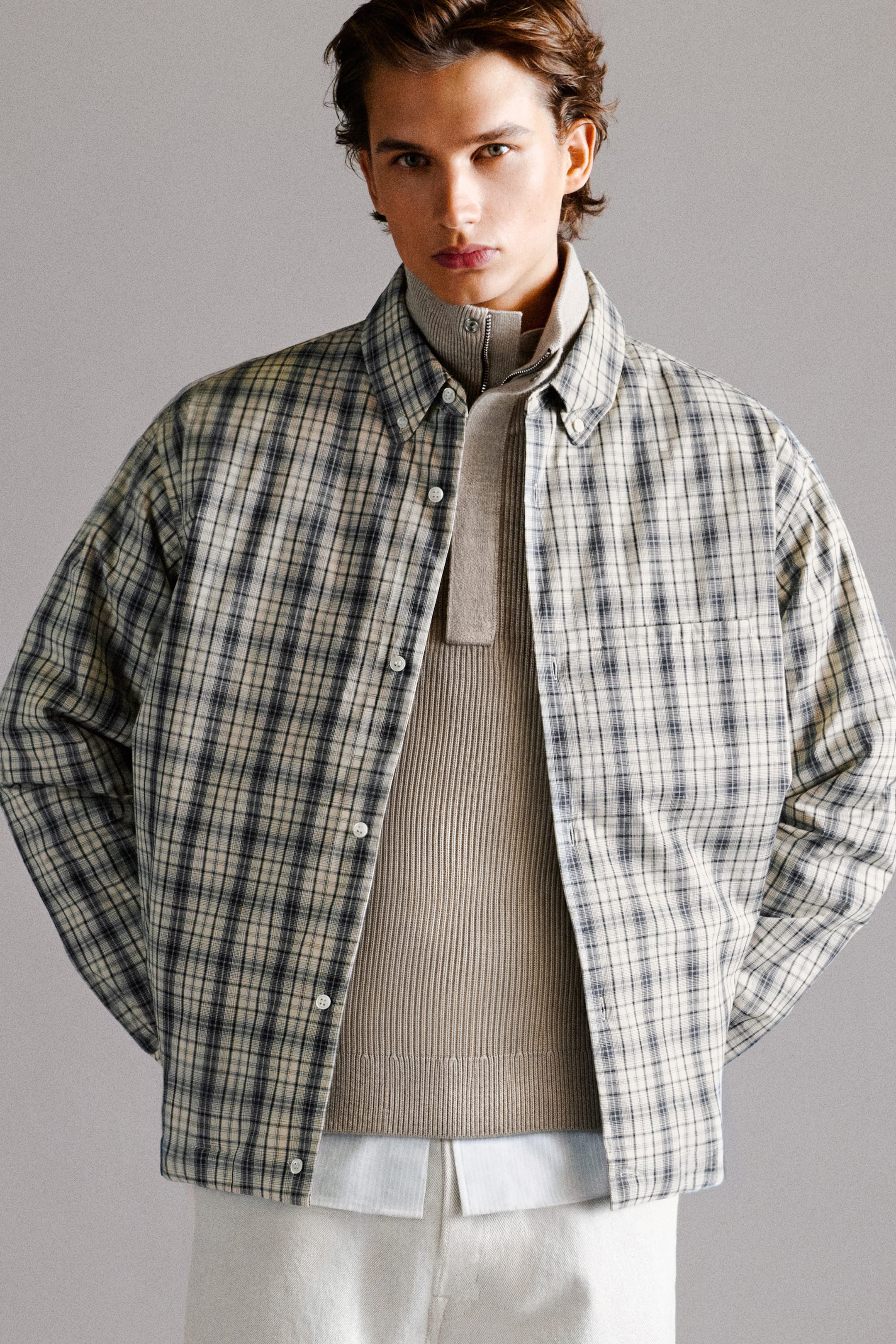 Das gesteppte Overshirt aus kariertem Baumwollstoff ist von vorne zu sehen und zeigt ein dezentes Karo-Muster in Creme, Grau und Schwarz. Es wird offen über einem beigen Ripp-Halbzip-Pullover getragen und hebt so seine lockere Passform, den Button-down-Kragen, den vorderen Knopfverschluss und die Brusttasche hervor. Das gesteppte Overshirt aus kariertem Baumwollstoff ist von vorne zu sehen und zeigt ein dezentes Karo-Muster in Creme, Grau und Schwarz. Es wird offen über einem beigen Ripp-Halbzip-Pullover getragen und hebt so seine lockere Passform, den Button-down-Kragen, den vorderen Knopfverschluss und die Brusttasche hervor.