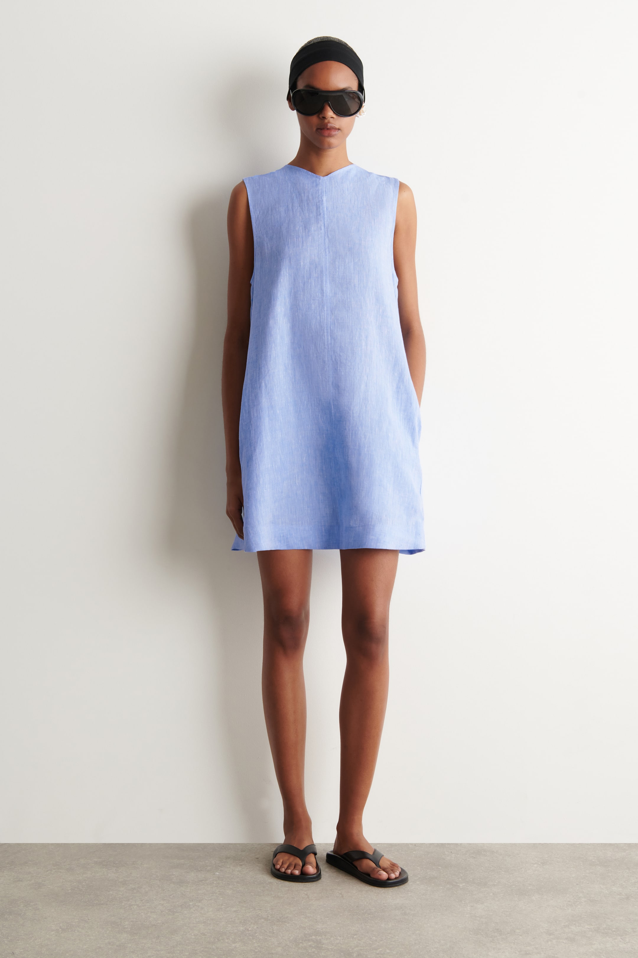 Ver imagem maior: Um vestido mini sem mangas azul claro apresenta um decote em V entalhado, uma silhueta em linha A solta, bolsos nas costuras laterais e uma costura vertical frontal.