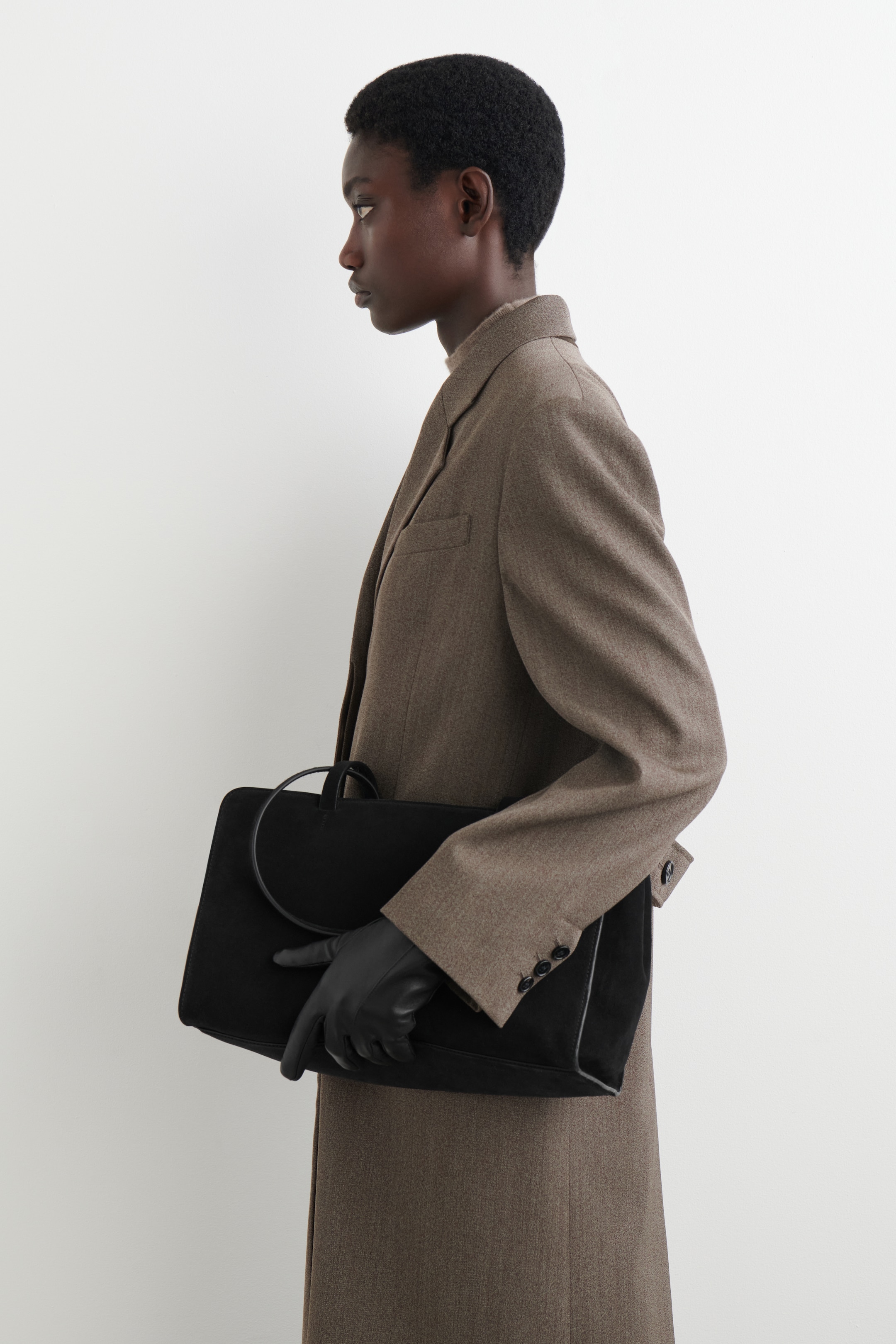 Ingrandisci l'immagine: Guanti in pelle nera sono indossati sulla mano sinistra, che tiene una borsa rettangolare nera.