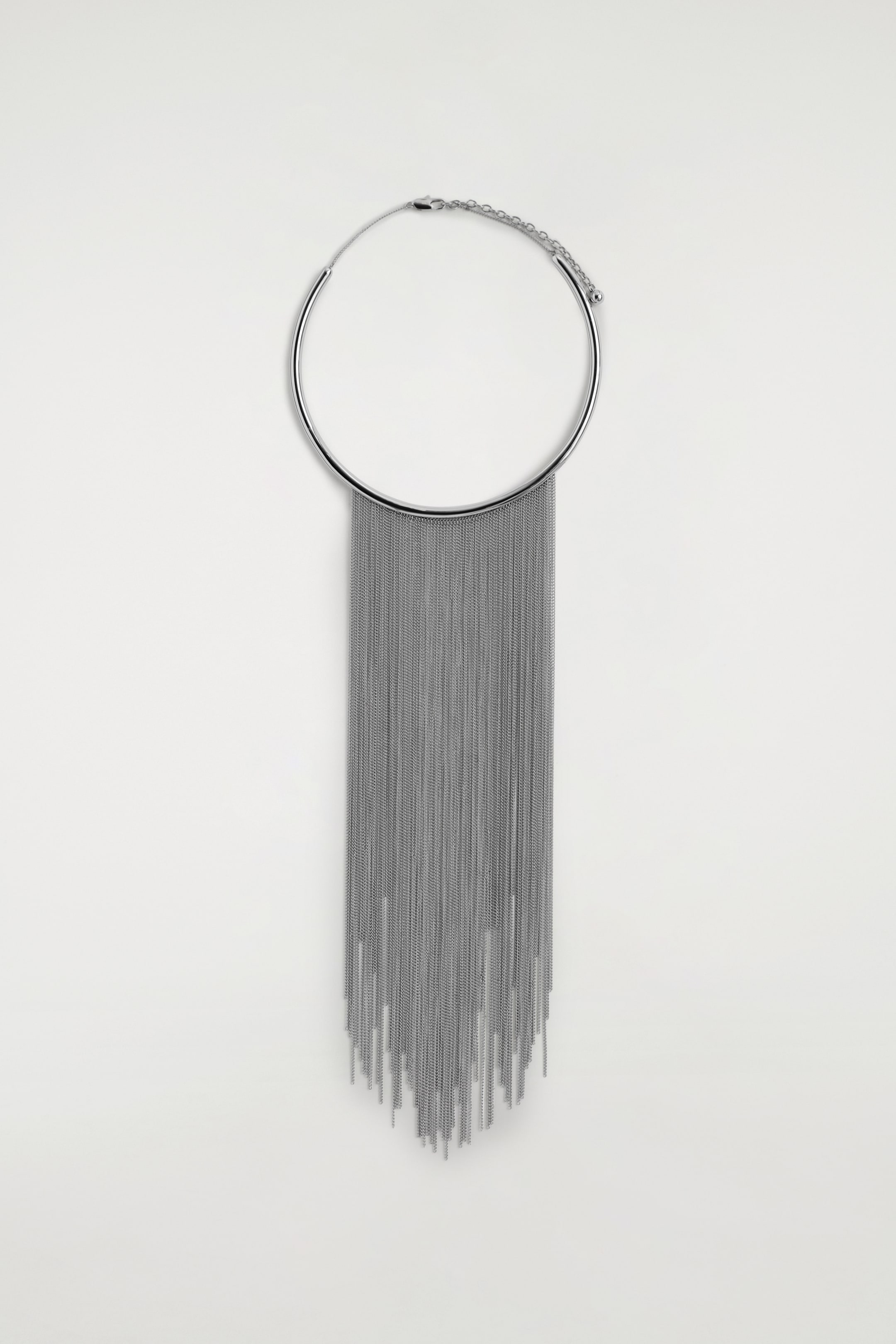 View larger image: A silver-toned necklace is presented front-facing, featuring a rigid, curved collar from which numerous thin chains are cascading downwards, forming a dense tassel. A lobster clasp with an extender chain is visible at the back of the collar.