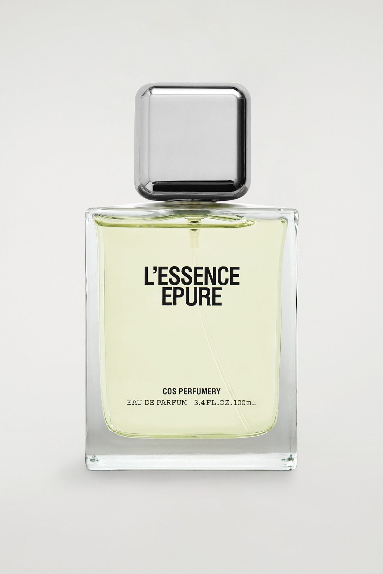 A rectangular glass bottle of COS Perfumery "L'Essence Epure" Eau de Parfum stands upright in a front-facing view, containing a pale yellow liquid. The bottle features a metallic, square-shaped silver cap with rounded corners and displays black printed text on the front reading "L'ESSENCE EPURE", "COS PERFUMERY", and "EAU DE PARFUM 3.4 FL.OZ. 100ml".
