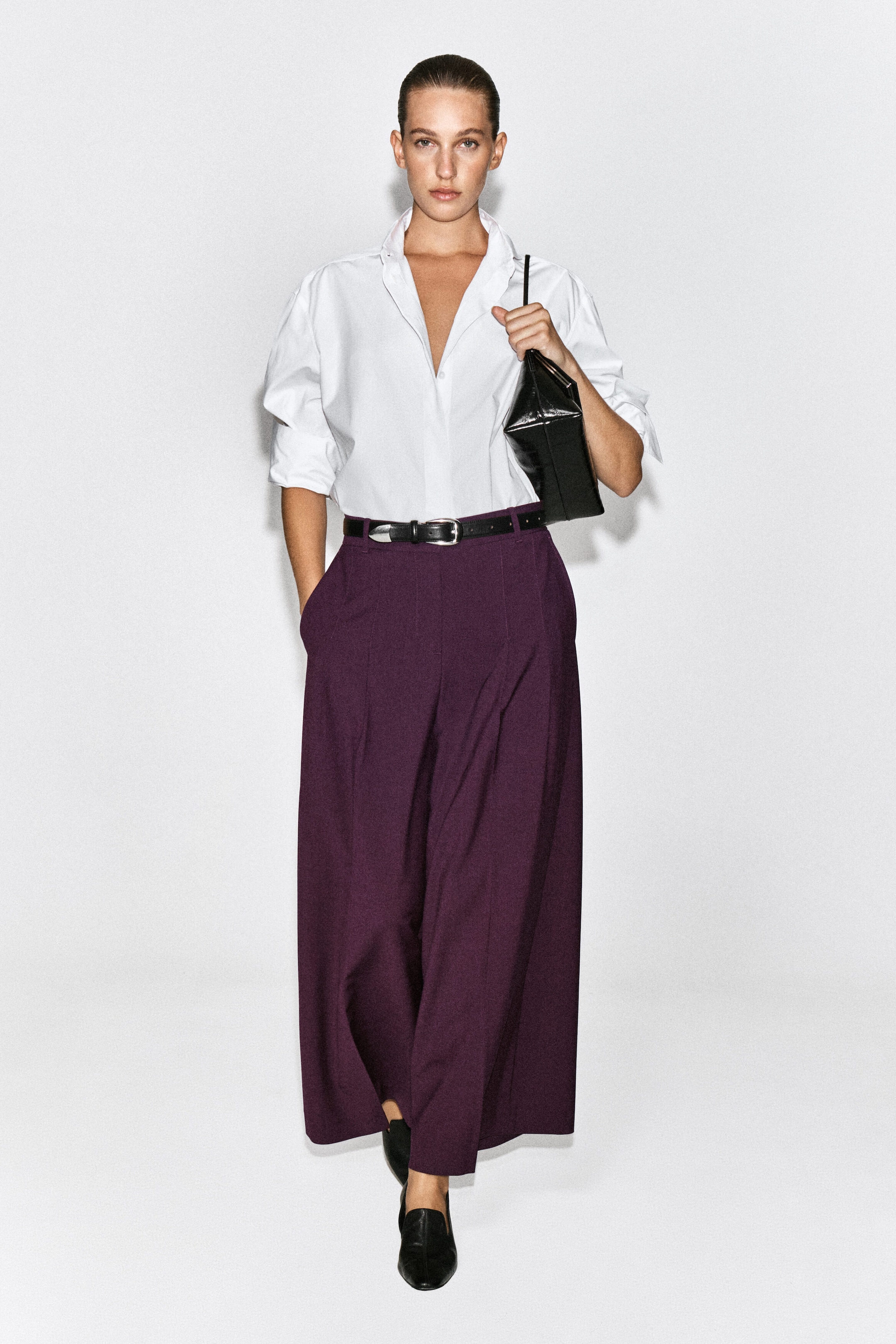 Pantaloni ampi in misto lana con pieghe in un intenso color prugna, indossati dalla modella, caratterizzati da vita alta, pieghe frontali e silhouette rilassata. I pantaloni sono abbinati a una camicia bianca con colletto infilata all’interno e a una cintura in pelle nera, mentre la modella è in posa con una mano nella tasca laterale. Pantaloni ampi in misto lana con pieghe in un intenso color prugna, indossati dalla modella, caratterizzati da vita alta, pieghe frontali e silhouette rilassata. I pantaloni sono abbinati a una camicia bianca con colletto infilata all’interno e a una cintura in pelle nera, mentre la modella è in posa con una mano nella tasca laterale.