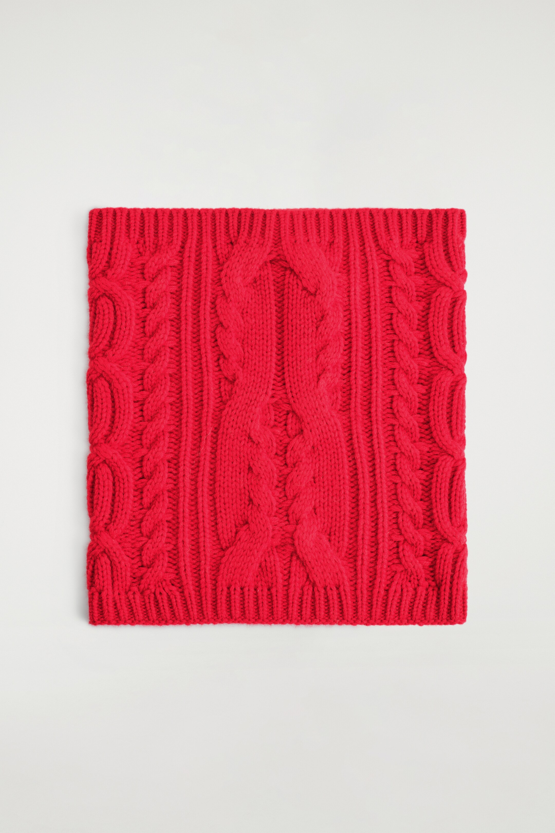 Agrandir l'image: Un snood rouge vif est présenté à l'AVANT, arborant un motif en tricot torsadé avec des rangées verticales de torsades, alternant avec des sections côtelées, et terminé par des bords côtelés.