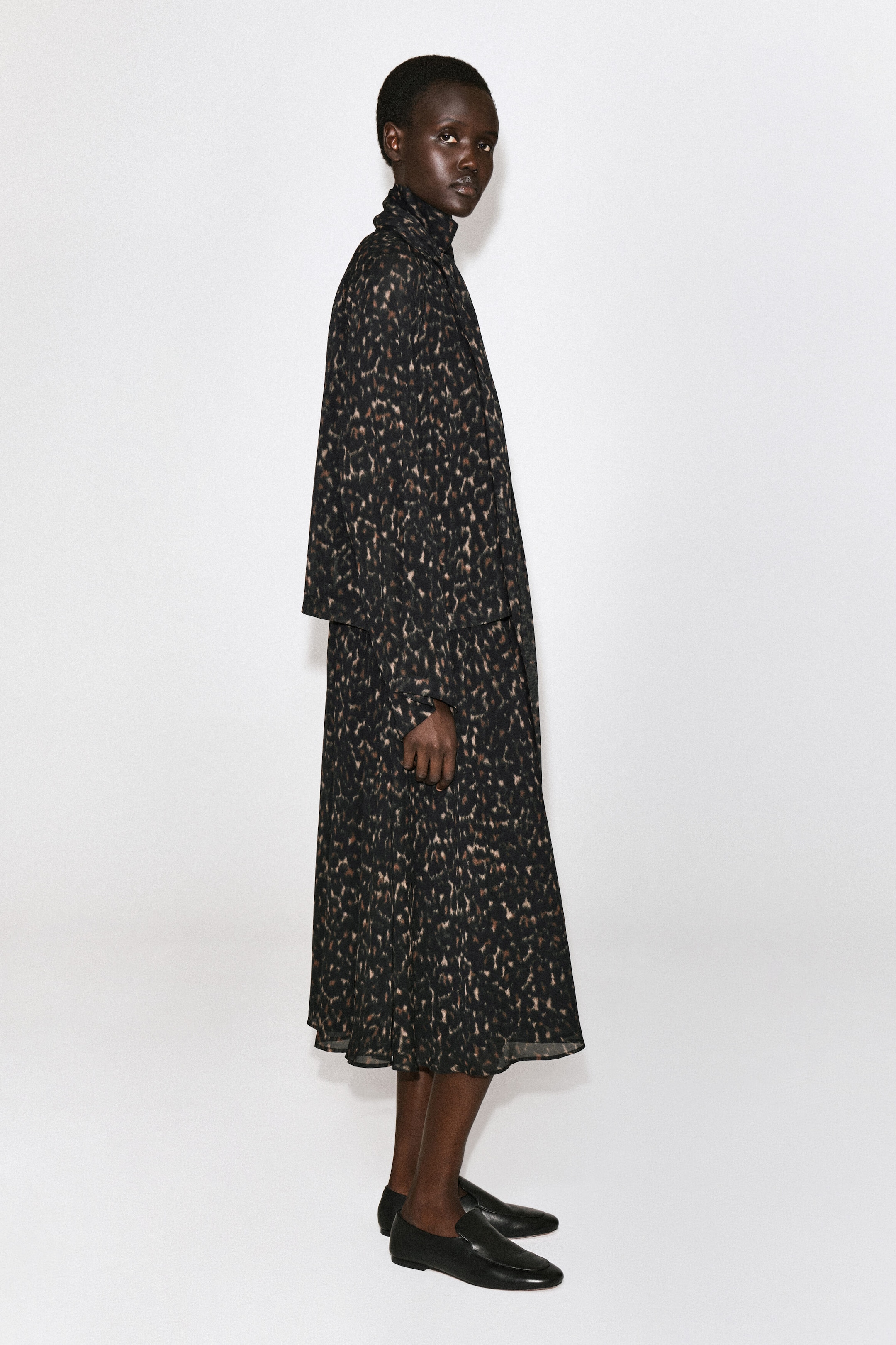 The leopard-print fluid scarf-detail dress is shown in a relaxed, midi-length silhouette, facing right to showcase its flowing design. It features a high-neck draped scarf collar, long sleeves with a cape-like back panel, and a lightweight, fluid skirt. The leopard-print fluid scarf-detail dress is shown in a relaxed, midi-length silhouette, facing right to showcase its flowing design. It features a high-neck draped scarf collar, long sleeves with a cape-like back panel, and a lightweight, fluid skirt.