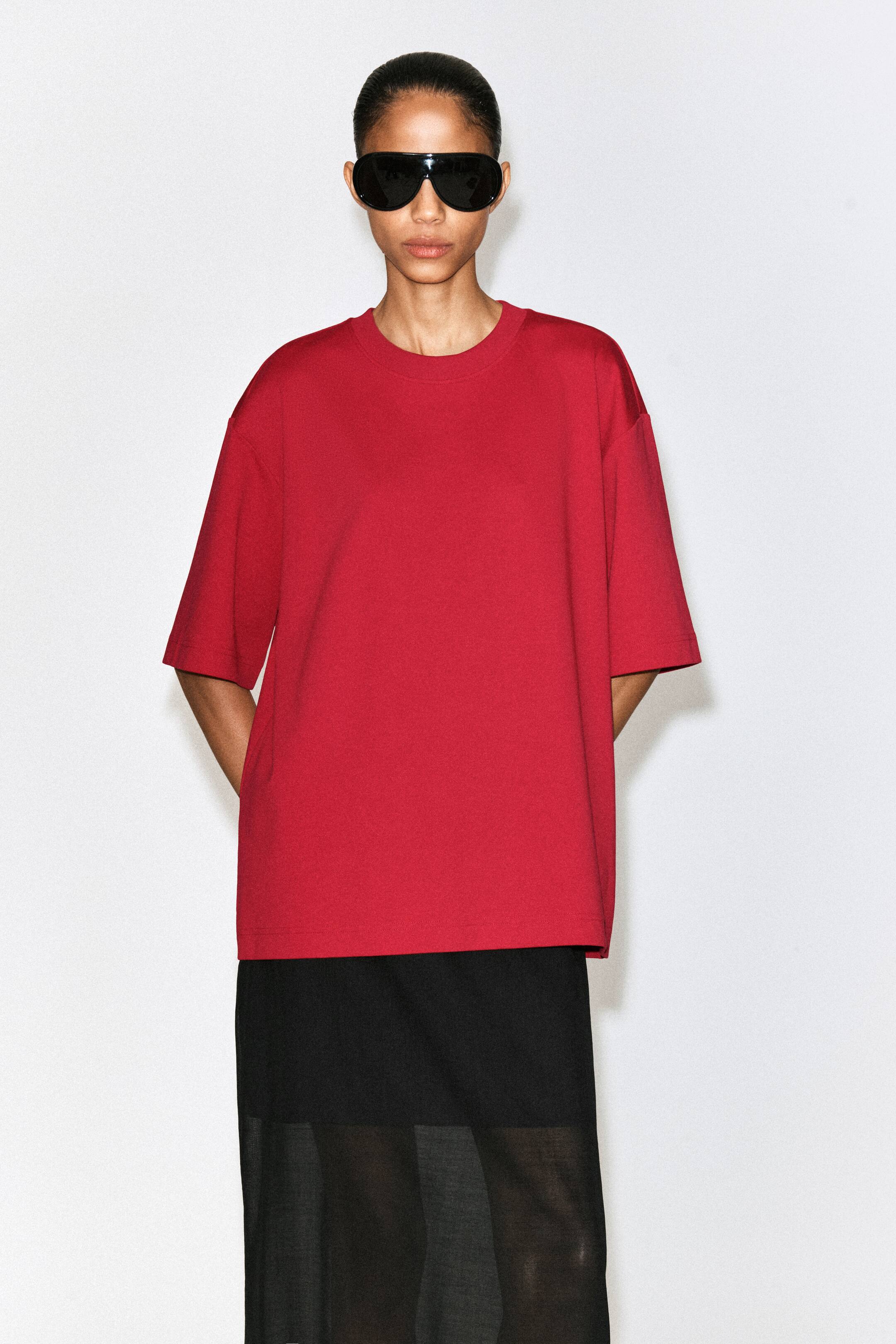 Zobacz większy obraz: Czerwony, oversize'owy t-shirt prezentowany jest od przodu, z prążkowanym dekoltem typu crew neck, przedłużonymi krótkimi rękawami oraz szerokim dołem, co tworzy luźny, swobodny krój.