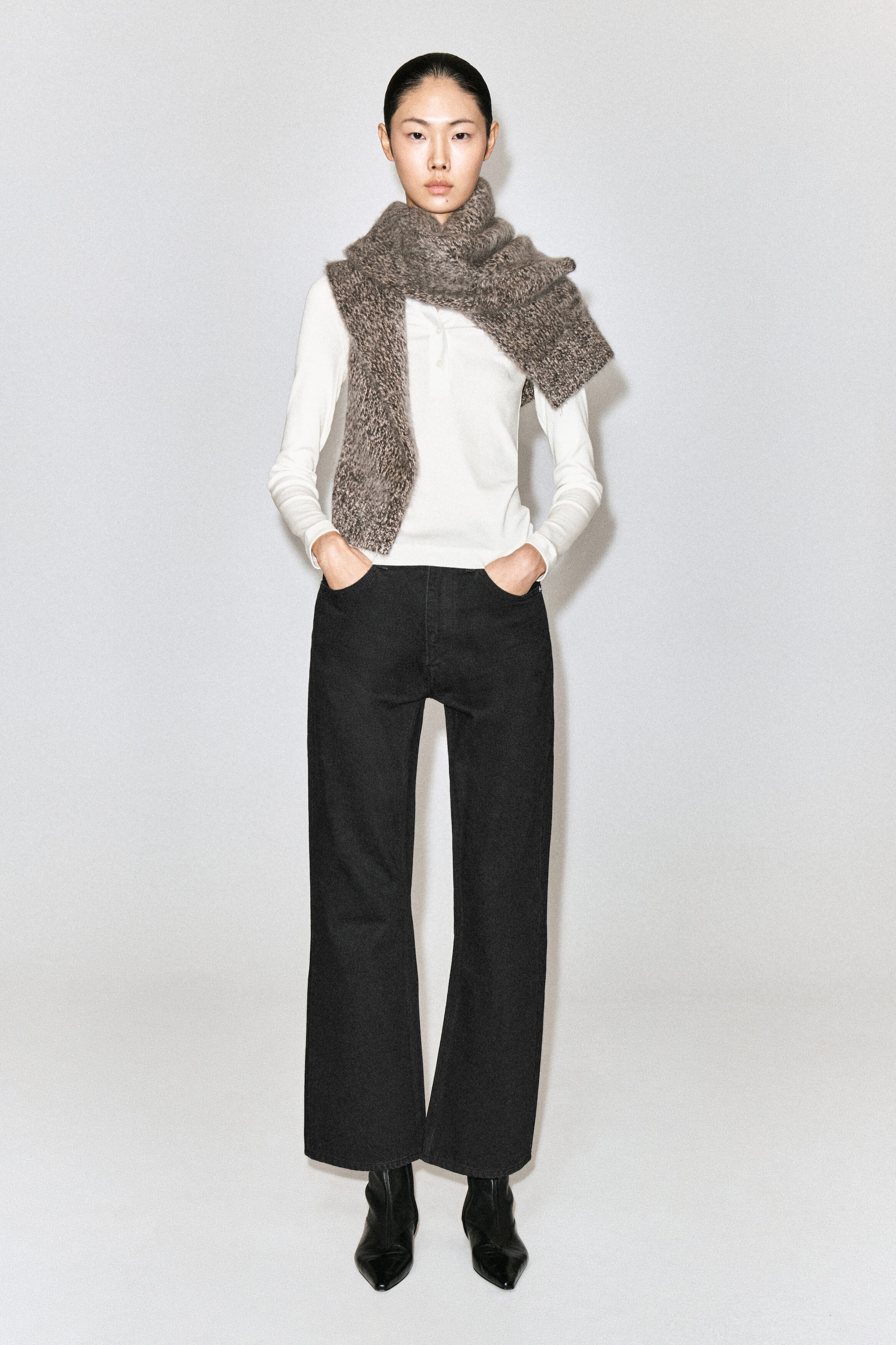 Le mannequin porte un jean noir bootcut, debout avec les mains dans les poches avant. Ce jean taille haute, longueur cheville, est associé à un haut blanc à manches longues, à une écharpe grise texturée en maille et à des bottines noires à bout pointu. Le mannequin porte un jean noir bootcut, debout avec les mains dans les poches avant. Ce jean taille haute, longueur cheville, est associé à un haut blanc à manches longues, à une écharpe grise texturée en maille et à des bottines noires à bout pointu.