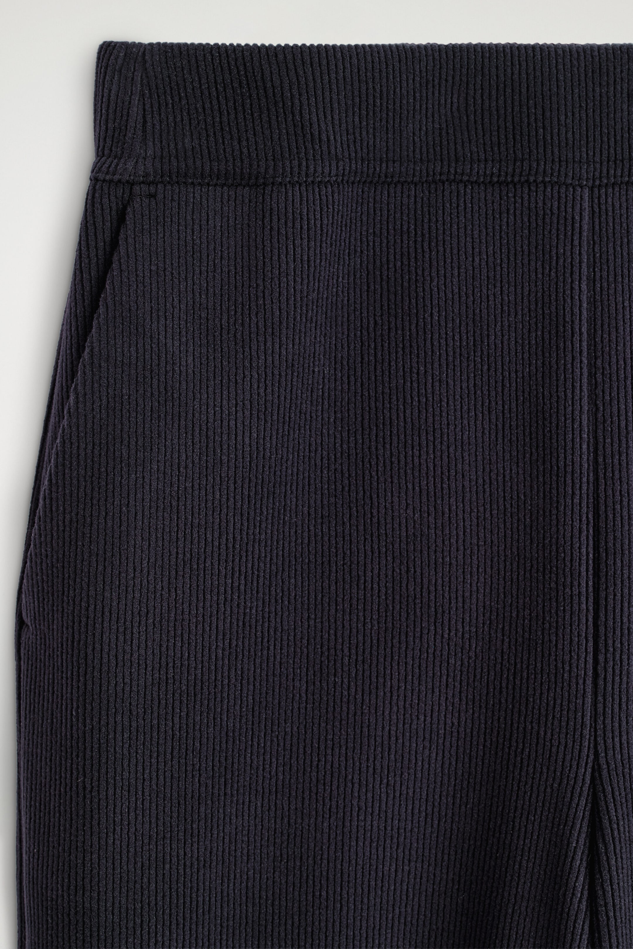 A close-up front view of the corduroy-jersey wide-leg pants showcases the dark navy fabric with its fine vertical ribbed texture. The design features a clean-finished waistband and a subtle side seam pocket.