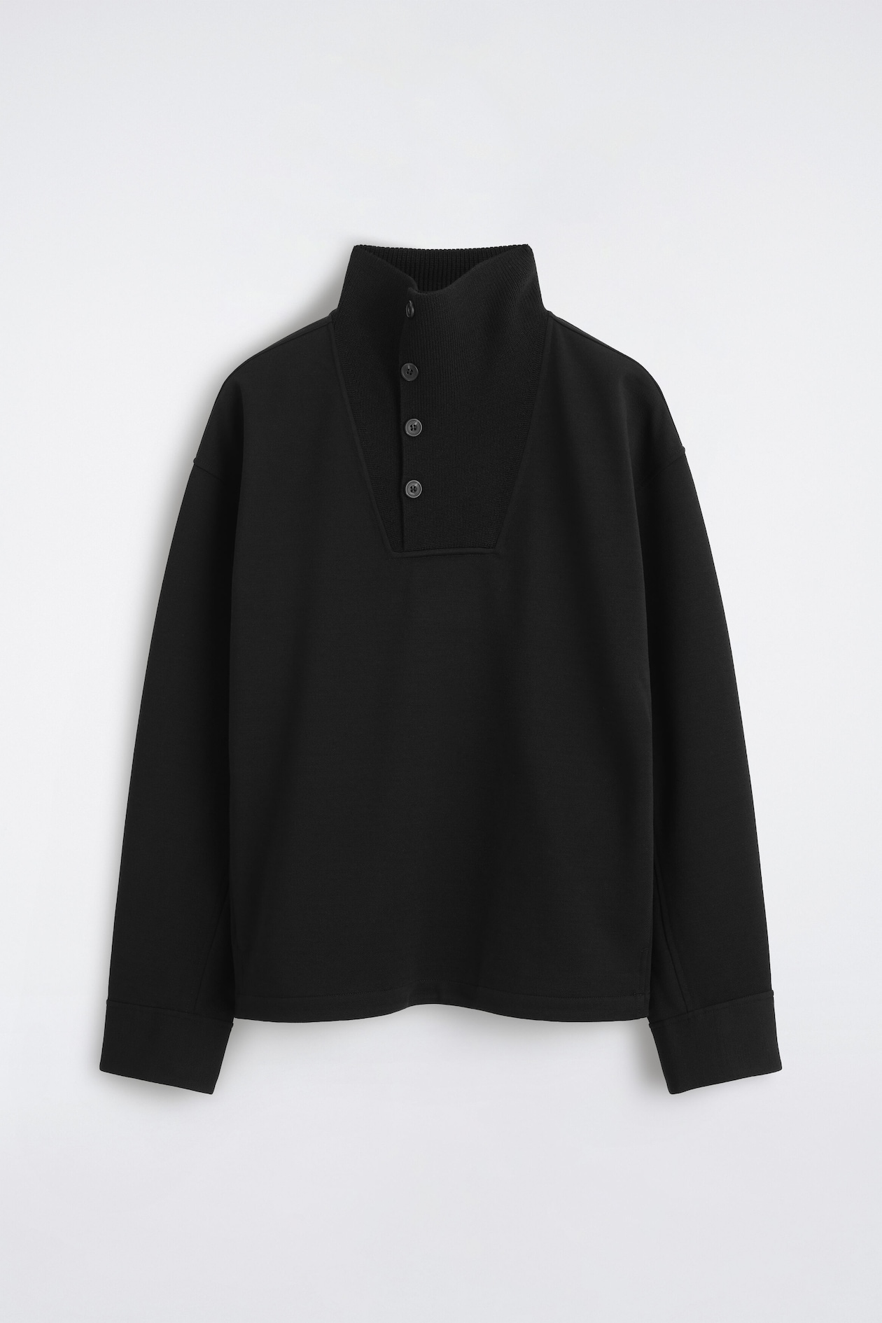 A black long-sleeve pullover is shown from the front, featuring a high mock neck with a ribbed knit panel and a four-button placket. The garment has a relaxed fit with dropped shoulders and wide, stitched cuffs.