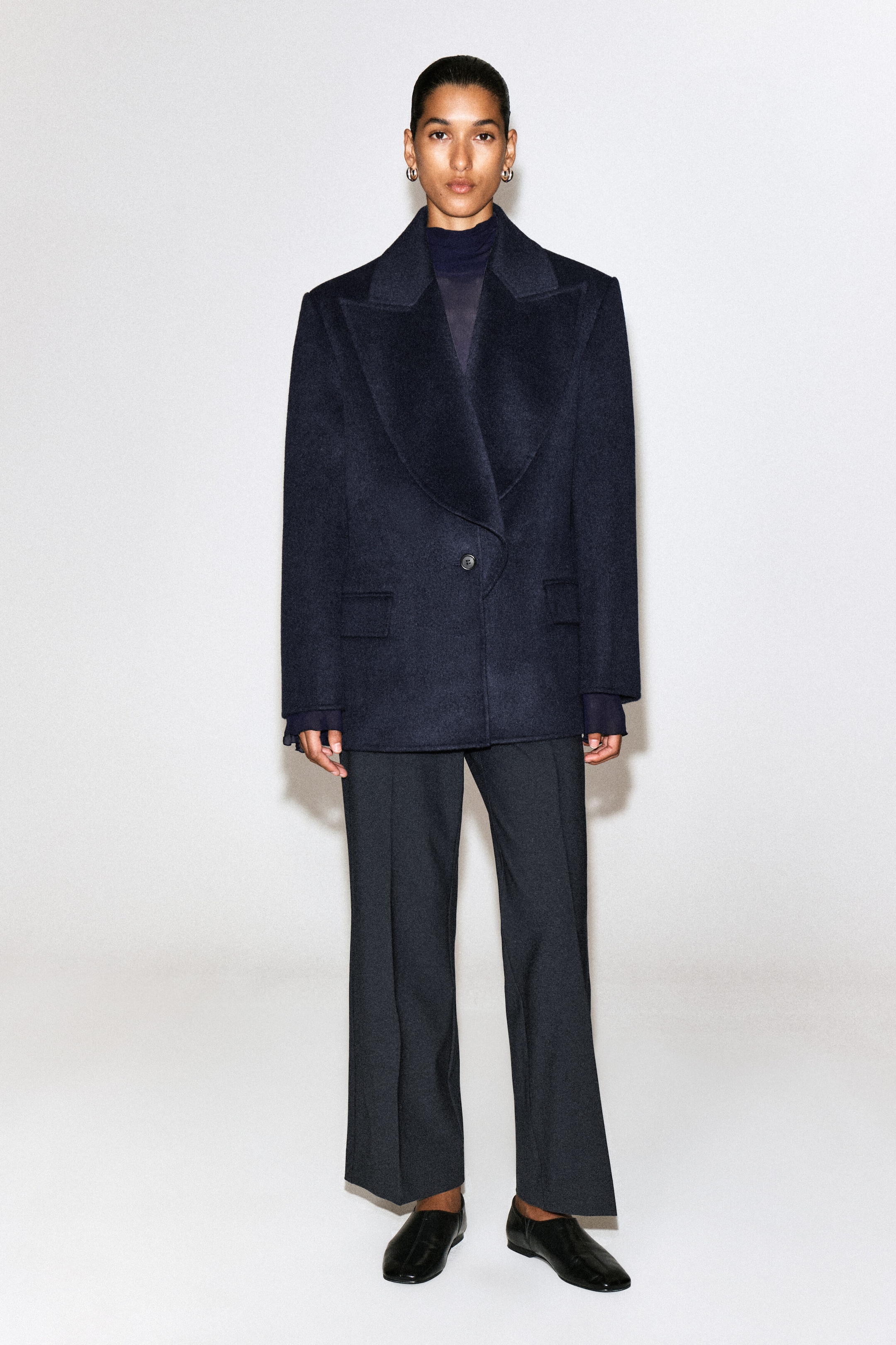 The twill cropped flared pants, shown from the front, drape in a relaxed fit with sharp pressed creases running down the center of each leg. They fall to a cropped length just above the ankle, showcasing a subtle flare at the hem.