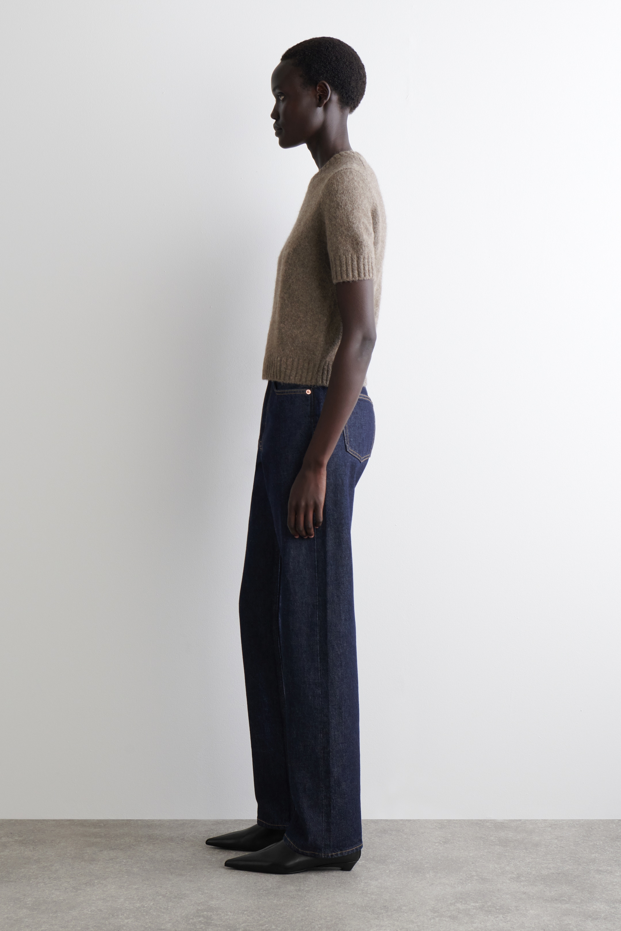 Agrandir l'image: Un pull en maille à manches courtes de couleur brun clair est présenté de profil, avec une texture duveteuse, des poignets côtelés et un ourlet côtelé qui s'arrête à la taille. Il est assorti à un jean à jambes larges de couleur foncée et des chaussures noires à talons bas et à bout pointu.
