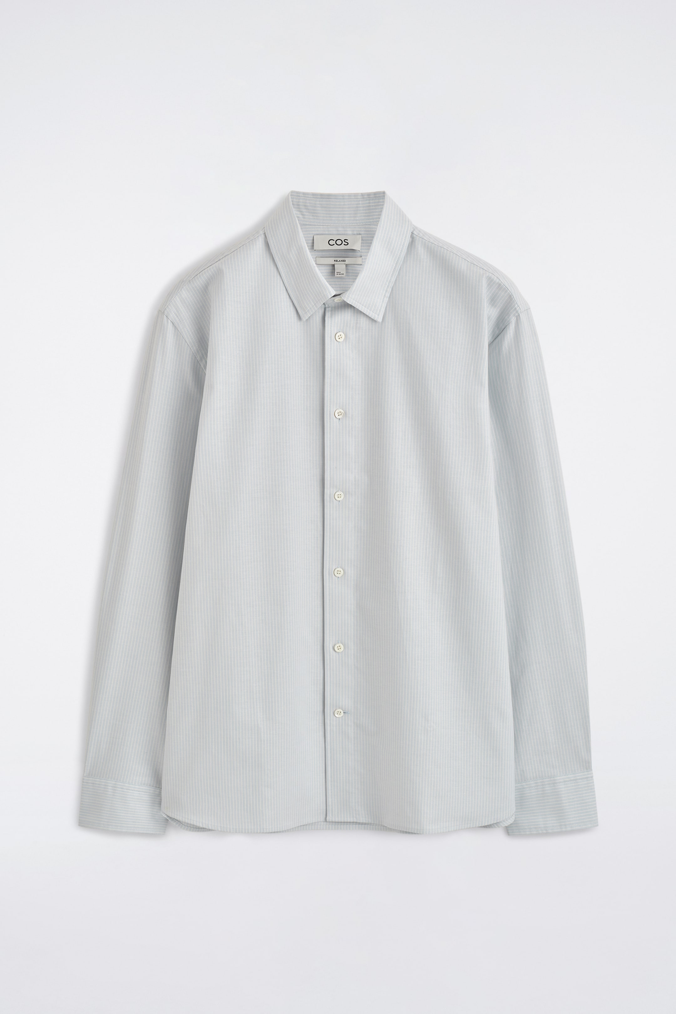 View larger image: An Oxford shirt in a pale blue hue with subtle vertical pinstripes is presented from the front, featuring a pointed collar, a full button-down placket with light-coloured buttons, long sleeves with single-button cuffs, and a curved hem.
