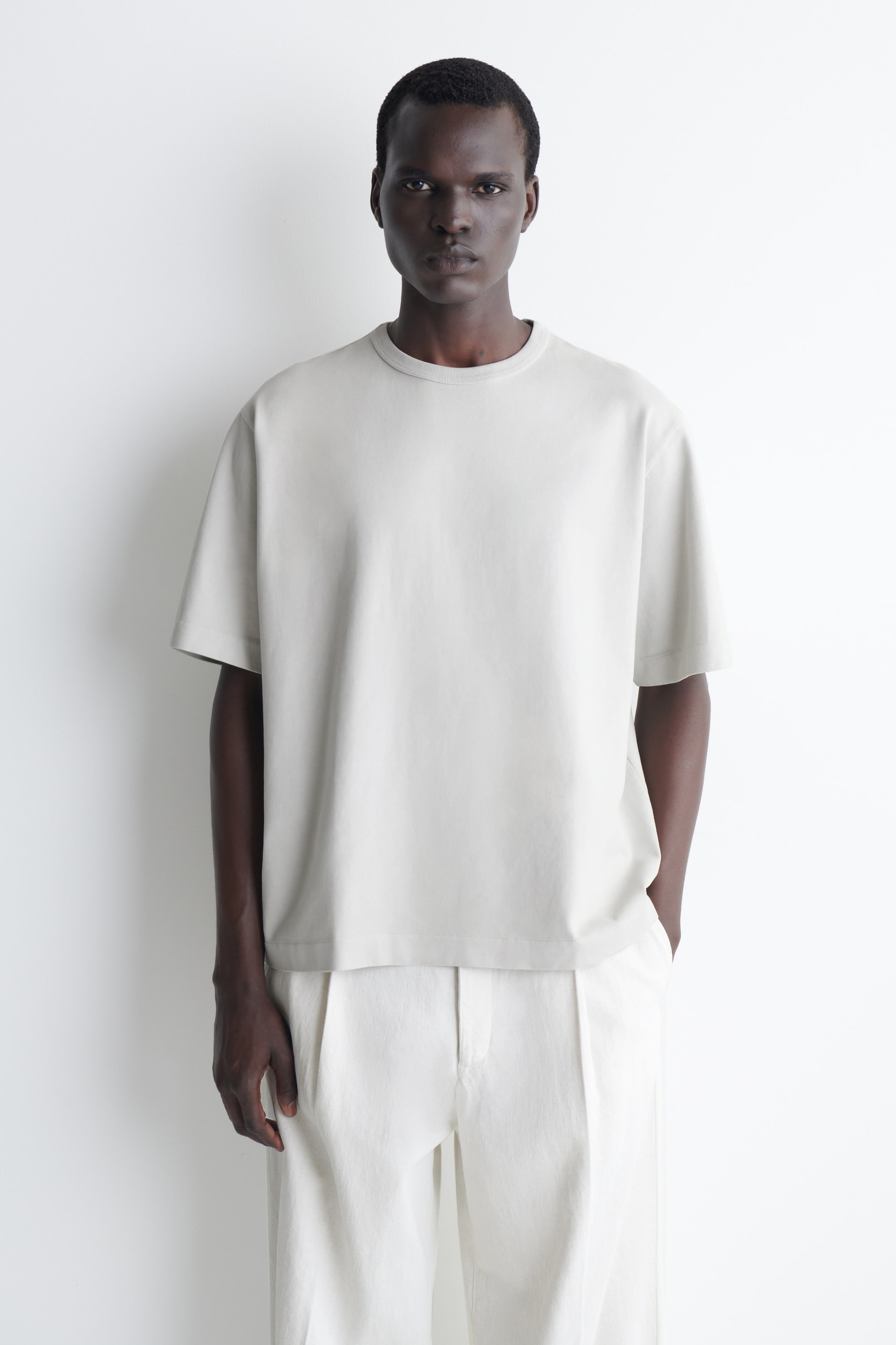 Agrandir l'image: Un t-shirt gris clair est porté, face avant. Il présente un col rond, des manches courtes et amples, et une coupe décontractée. L'ourlet droit repose à la taille.