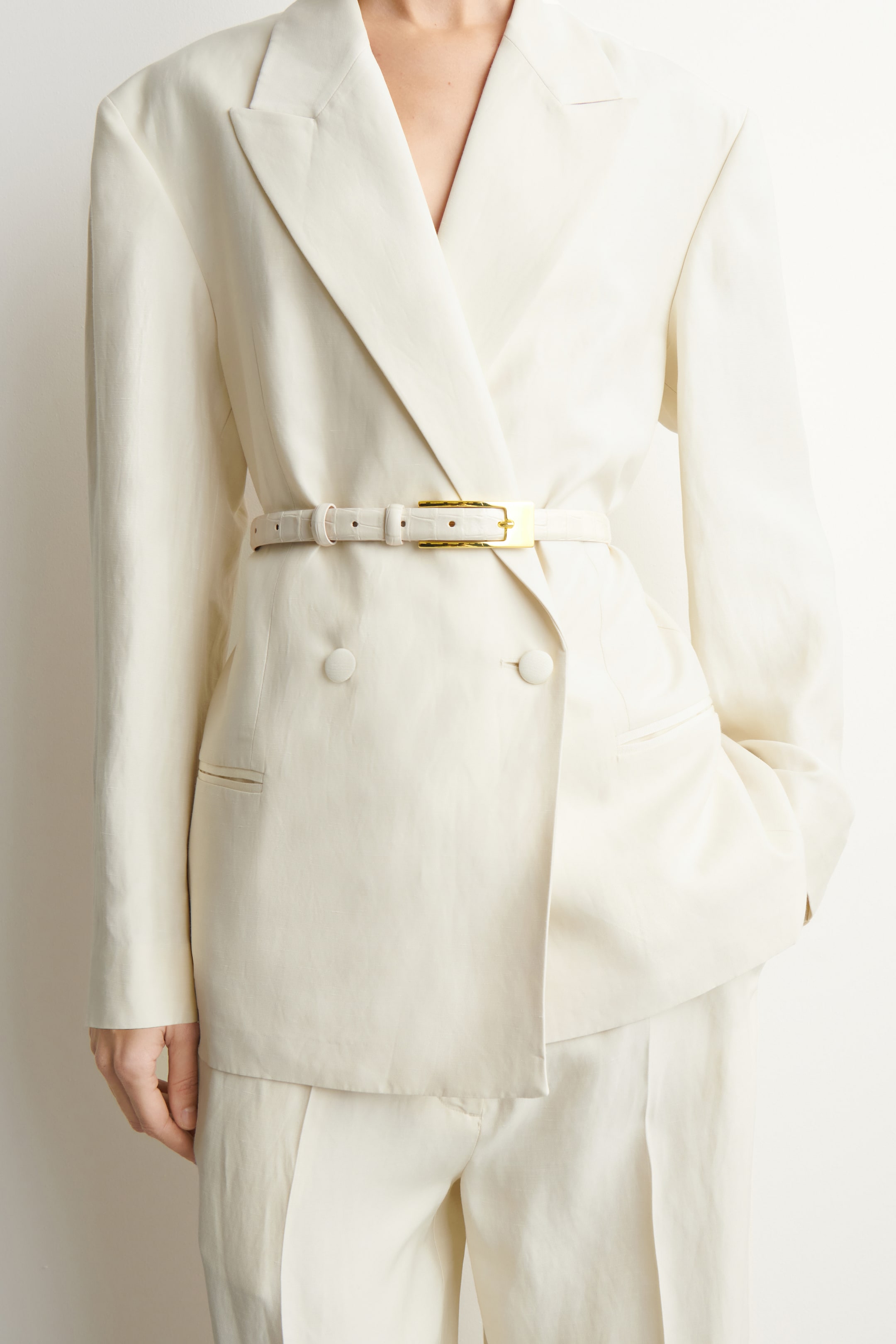 Agrandir l'image: Une ceinture étroite en cuir gaufré couleur crème est portée par le mannequin, cintrant la taille d'un blazer crème à double boutonnage. Elle est dotée d'une boucle rectangulaire allongée de ton doré.