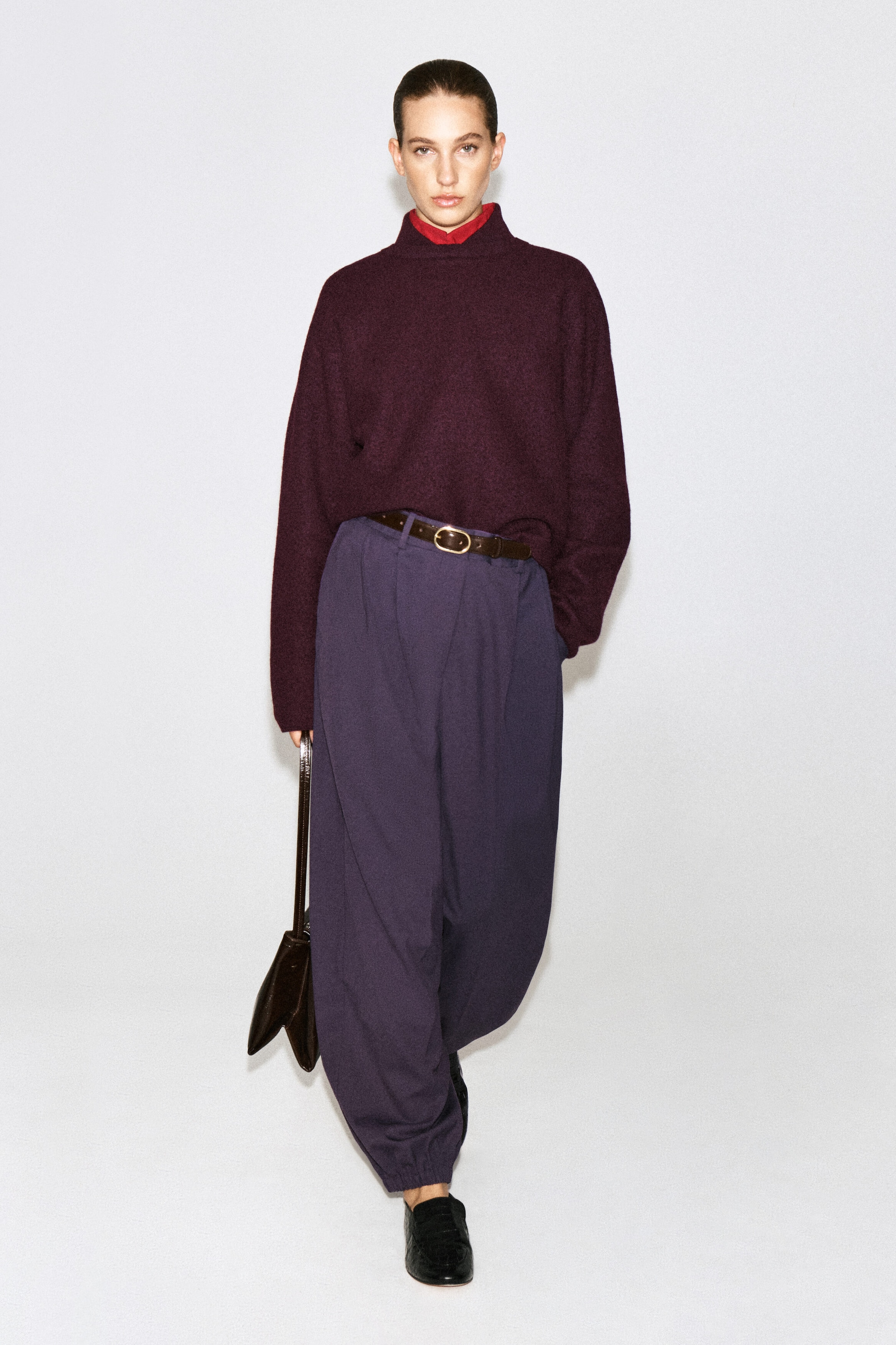Un chandail en laine bouillie bordeaux foncé, doté d’un col montant à couches superposées avec une sous-couche rouge, est porté par le mannequin. Le chandail est rentré dans un pantalon violet taille haute à jambe large, rehaussé d’une ceinture brune, tandis que le mannequin porte un sac à main brun foncé. Un chandail en laine bouillie bordeaux foncé, doté d’un col montant à couches superposées avec une sous-couche rouge, est porté par le mannequin. Le chandail est rentré dans un pantalon violet taille haute à jambe large, rehaussé d’une ceinture brune, tandis que le mannequin porte un sac à main brun foncé.