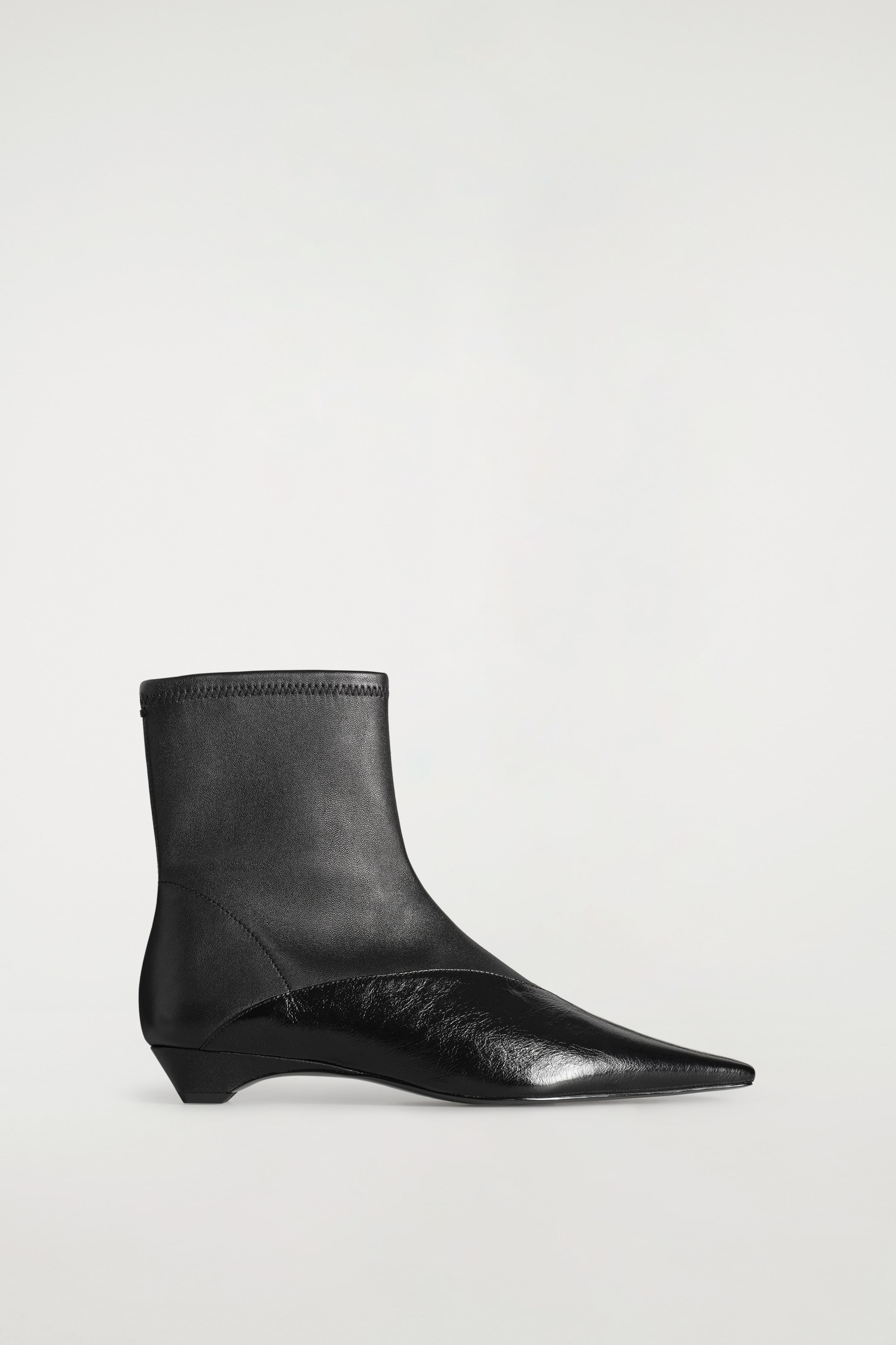 Grösseres Bild ansehen: Ein schwarzer, in Paneele unterteilter Leder-Wedge-Stiefelette mit spitzer Spitze wird im Seitenprofil gezeigt und verfügt über einen glatten, matten Leder-Schafteintritt am Knöchel sowie ein kontrastierendes, geknittertes Lackleder-Vorderblatt, das in eine scharf zulaufende Spitze übergeht.