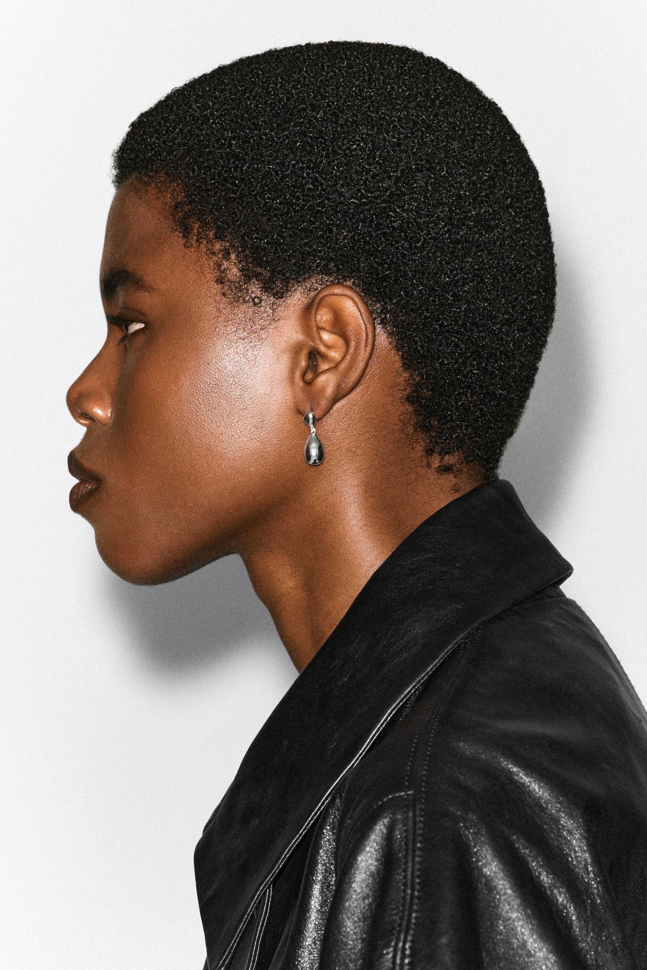 Mismatched drop earrings, featuring a polished silver teardrop-shaped pendant, are worn by the model in her earlobe. The earring is styled with a black leather jacket.