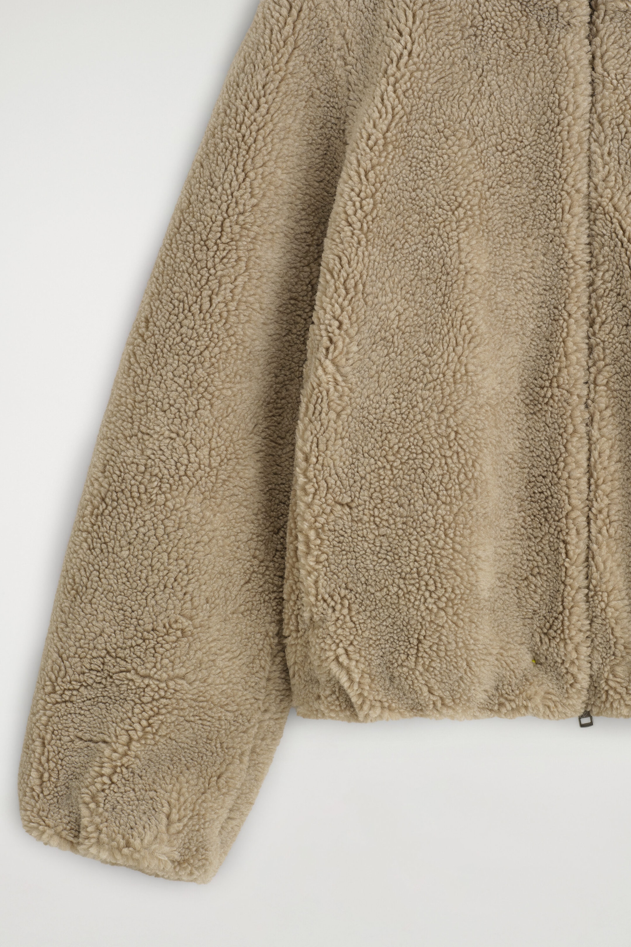 The funnel-neck teddy jacket is shown in a close-up front view, highlighting its textured beige sherpa fleece fabric. The jacket features a long sleeve with a gathered cuff and a front zipper closure visible at the hem.